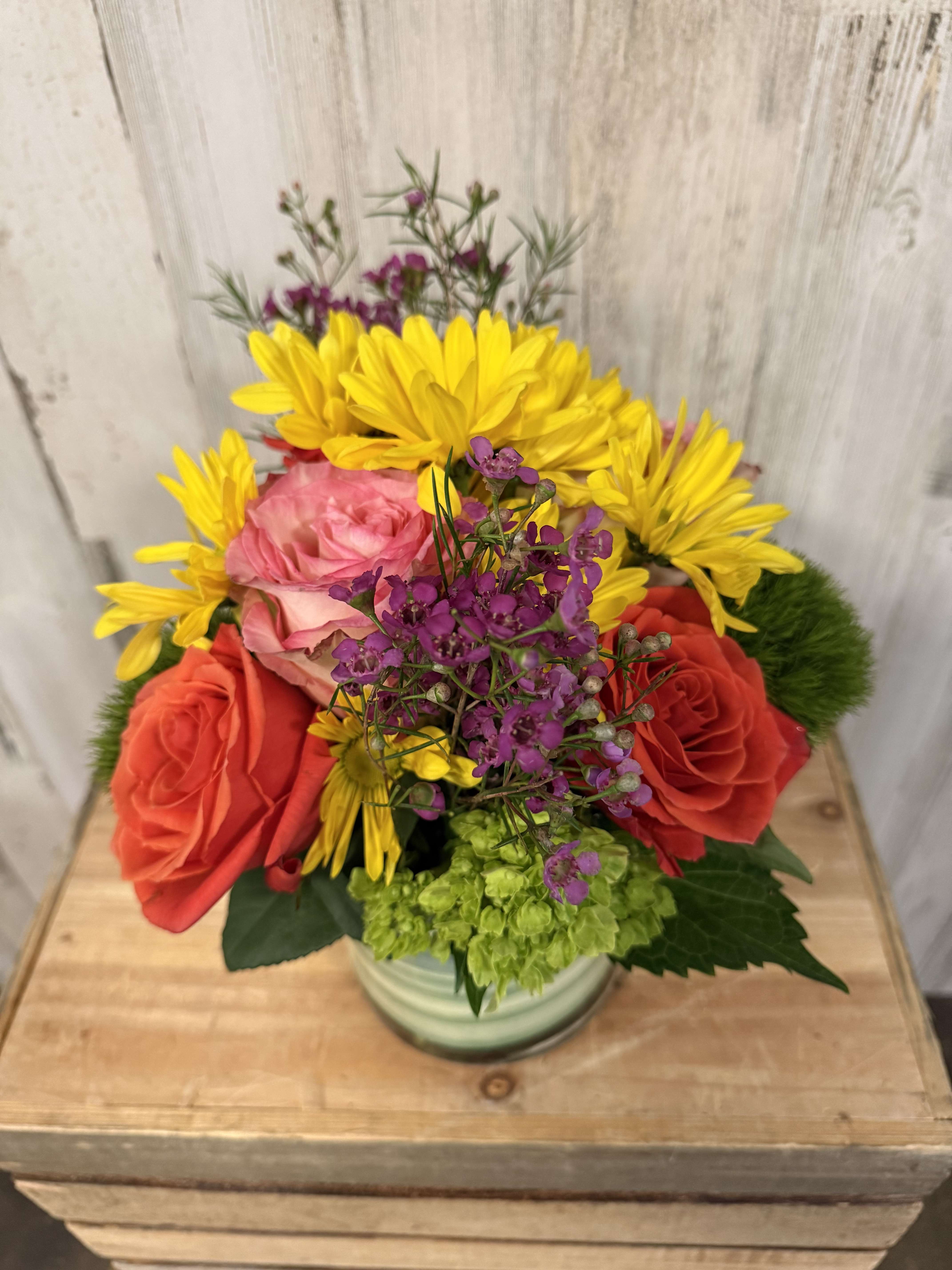 Mixed bouquet of roses, yellow daisies, and purple filler flowers in a vase