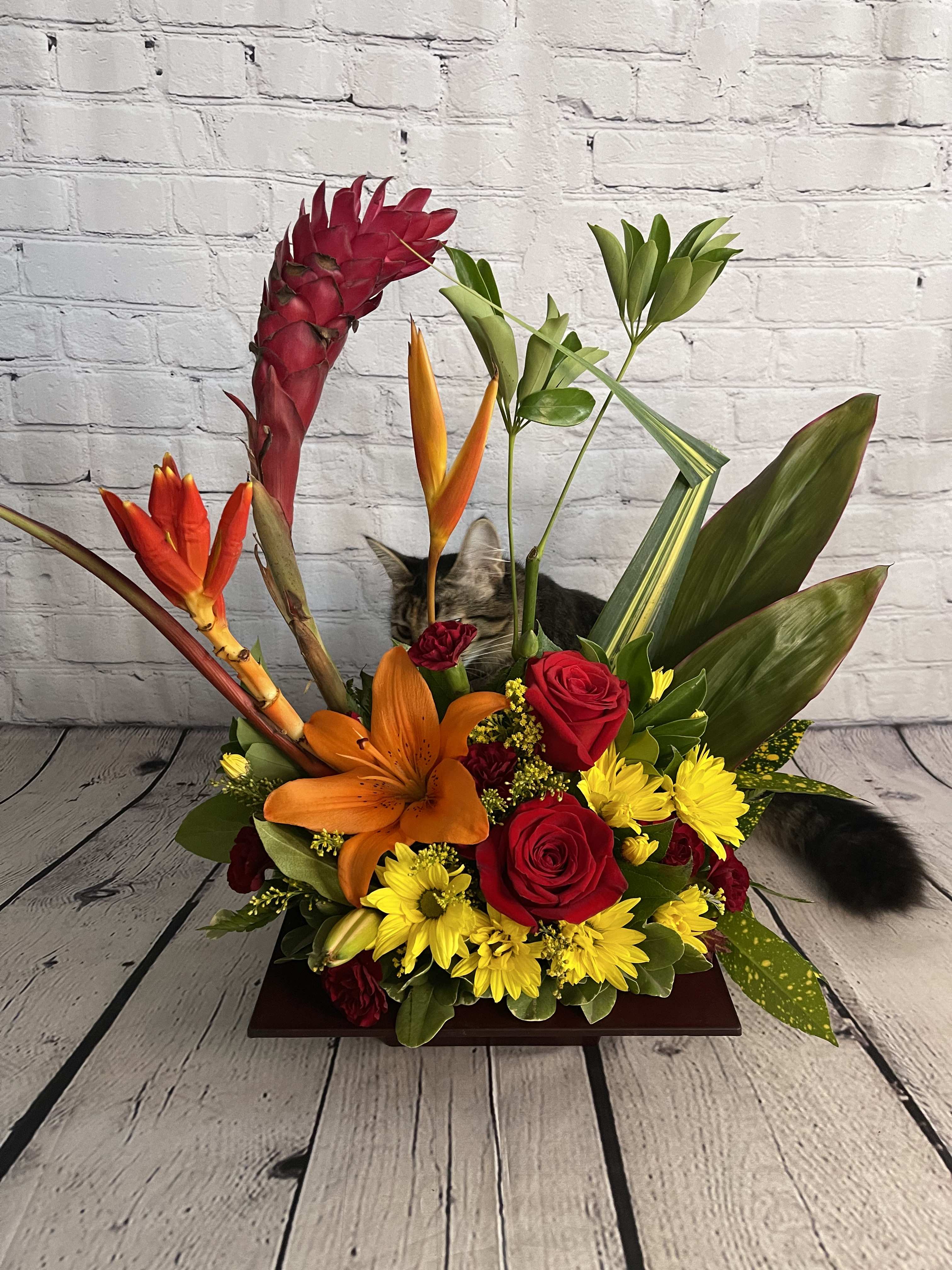 Tropical flower arrangement with red roses, orange lily, and yellow daisies in a low wooden base