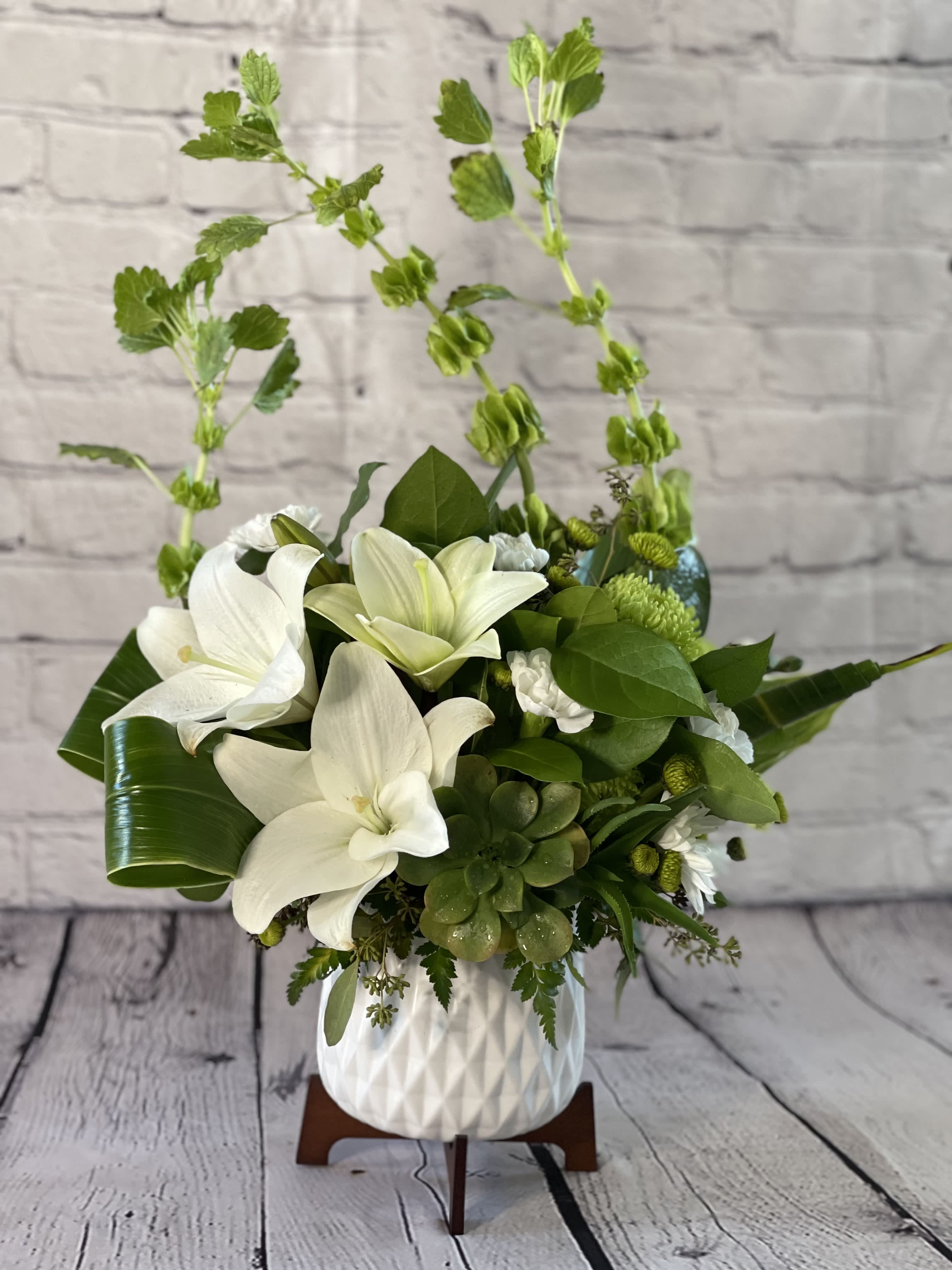 White lilies and green succulents arranged in a white vase