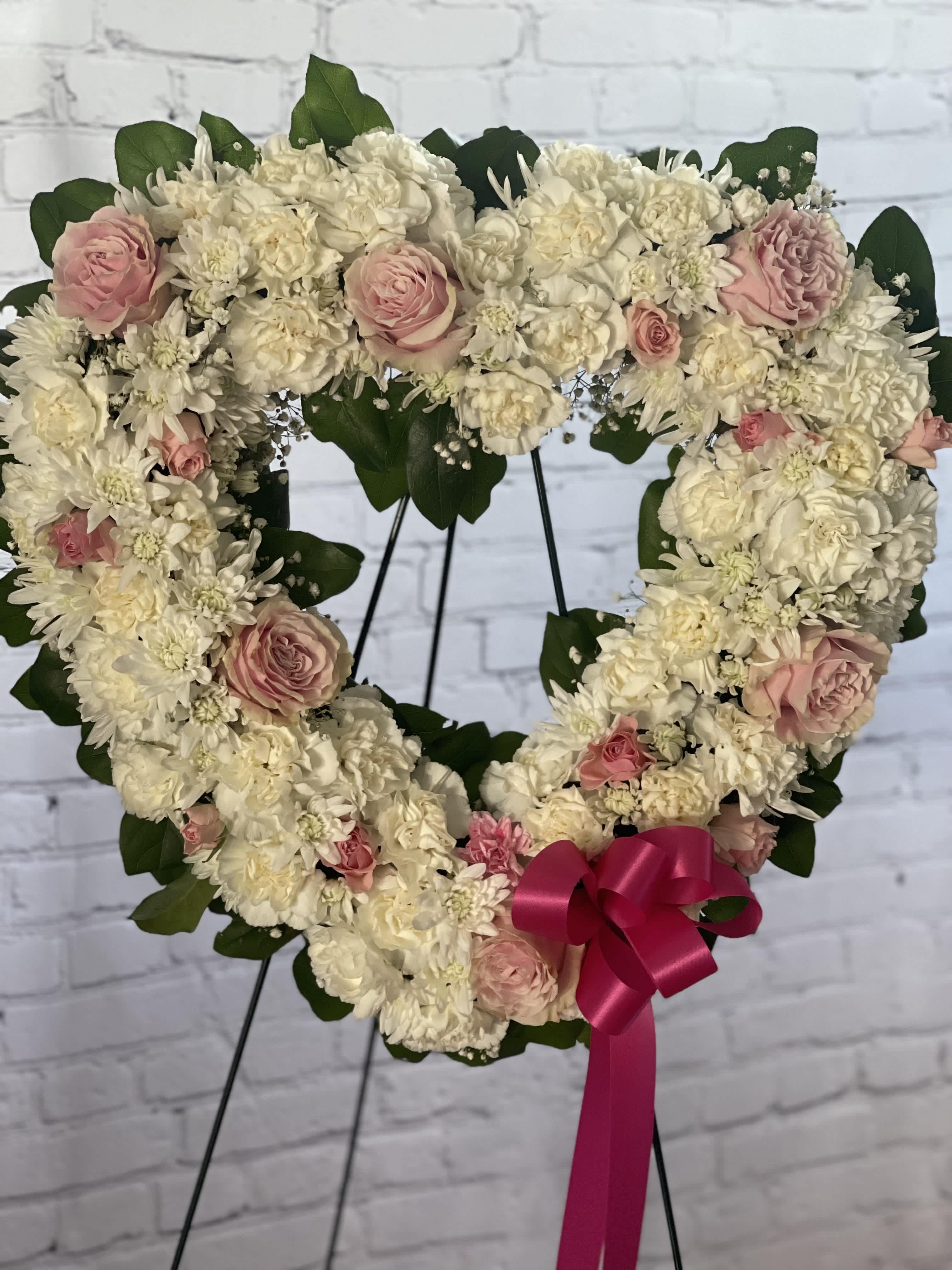 Heart-shaped floral wreath of white and pink flowers with a ribbon bow