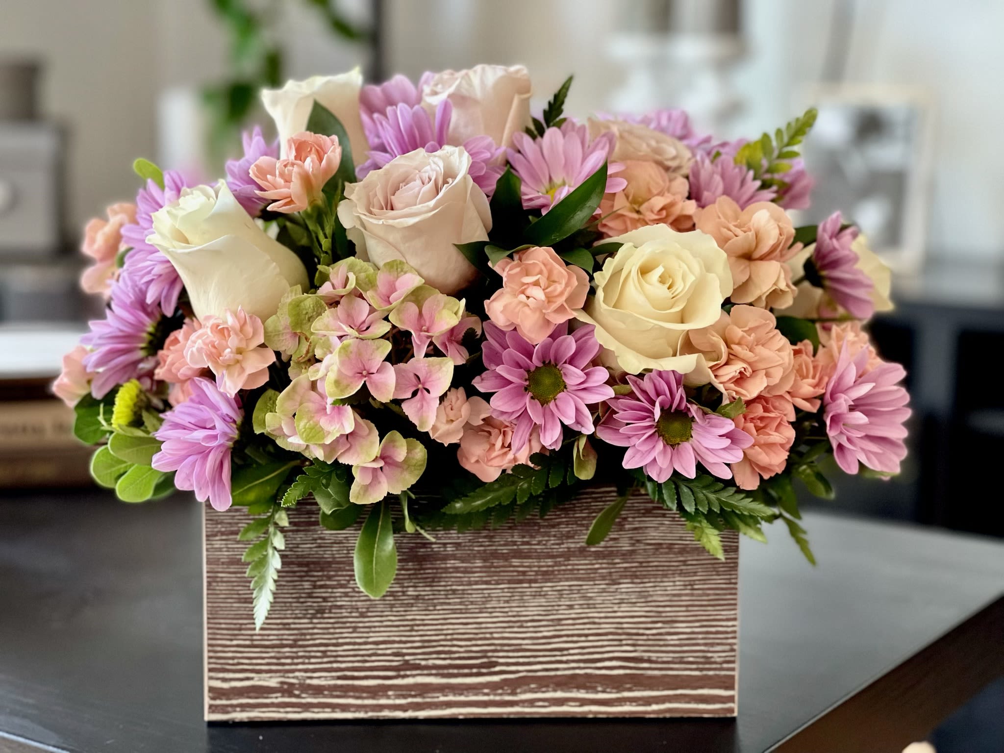 Pastel roses, daisies, carnations, and hydrangea arranged in a rustic wooden box