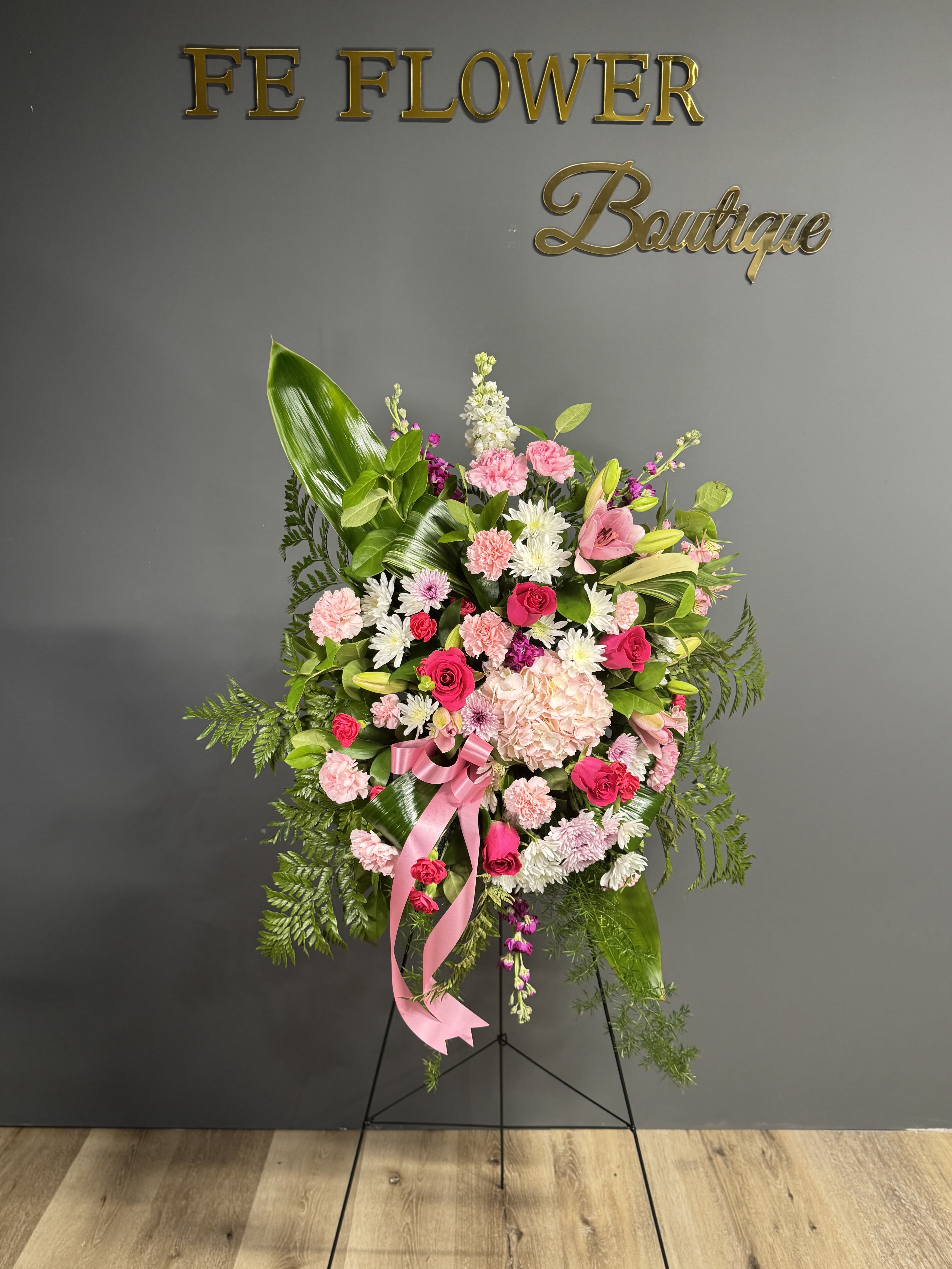 Pink and white floral standing spray with a pink ribbon on an easel