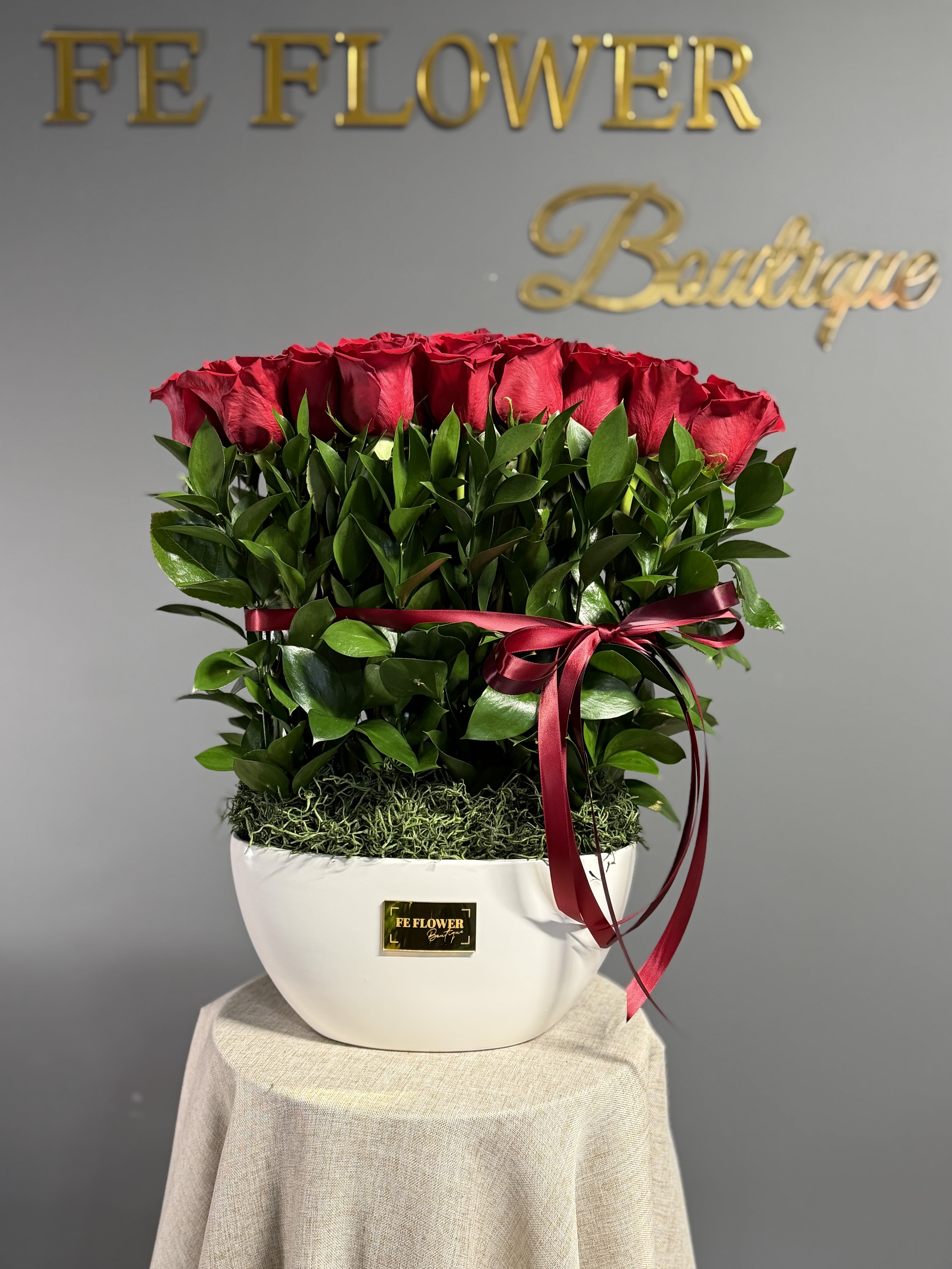 Red roses arranged in a white vase with a burgundy ribbon