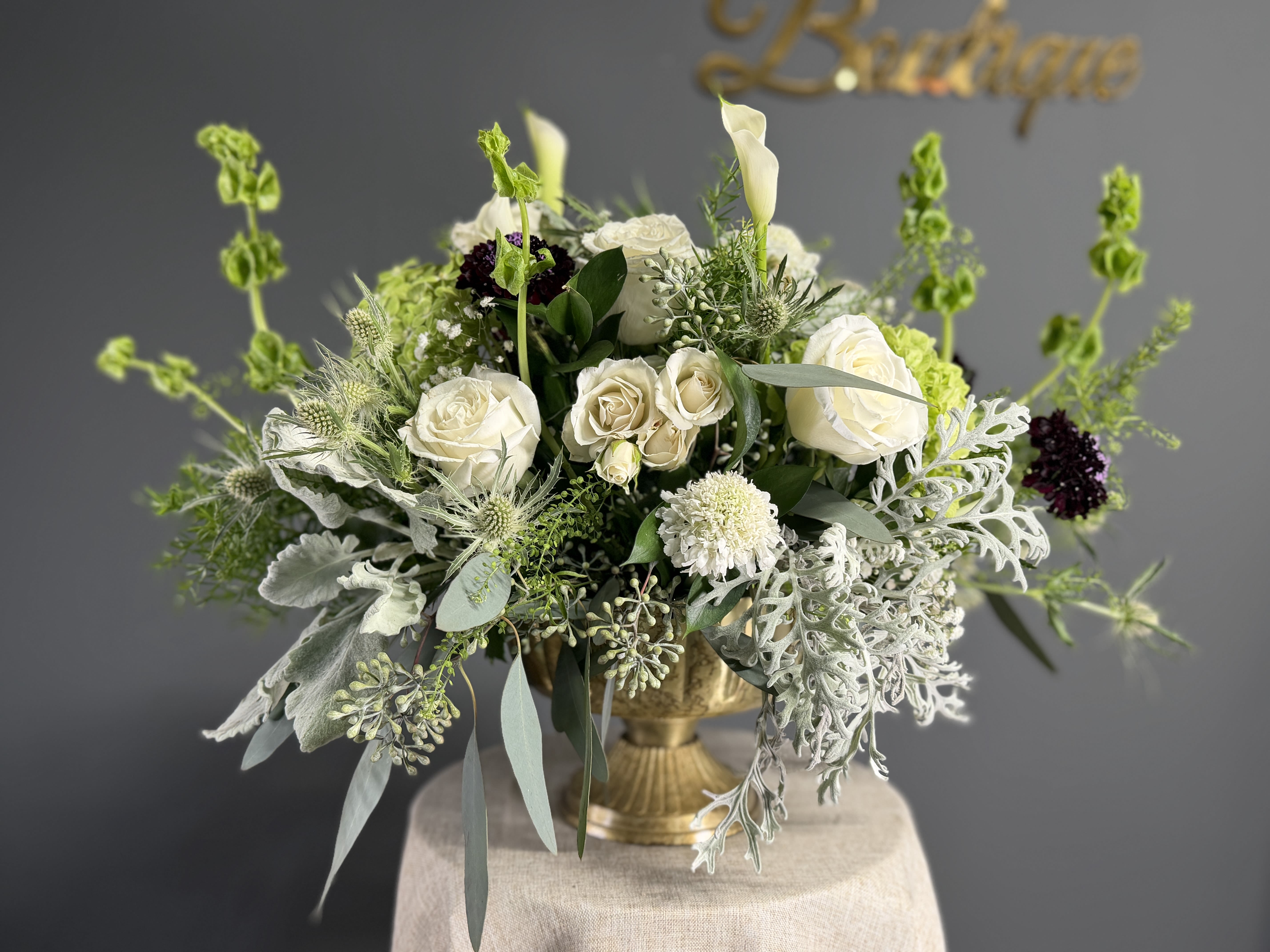 Rustic Elegance - A naturally refined arrangement that blends soft whites and fresh greens for a timeless, organic look. Featuring delicate roses, hydrangeas, and textured seasonal foliage in a golden metal vessel. Rustic Elegance brings a perfect balance of sophistication and countryside charm ideal for thoughtful gifts or elegant spaces.  **If you’d like to add a touch of color, simply let us know your preferred rose color in the Special Instructions box at checkout. **