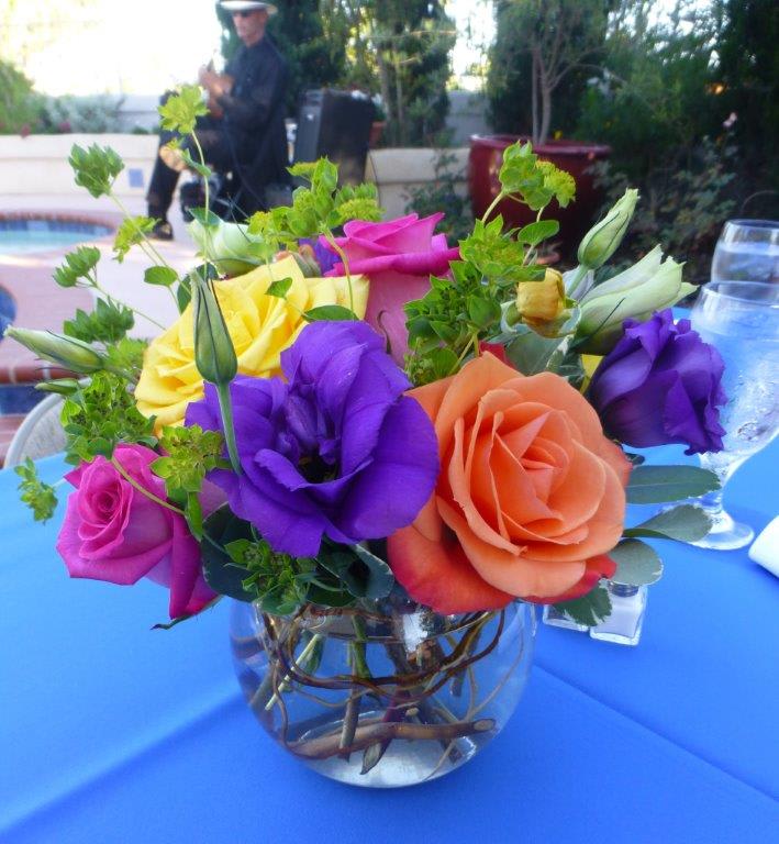 Small round centerpiece with orange, yellow, pink, and purple flowers in a clear bowl vase