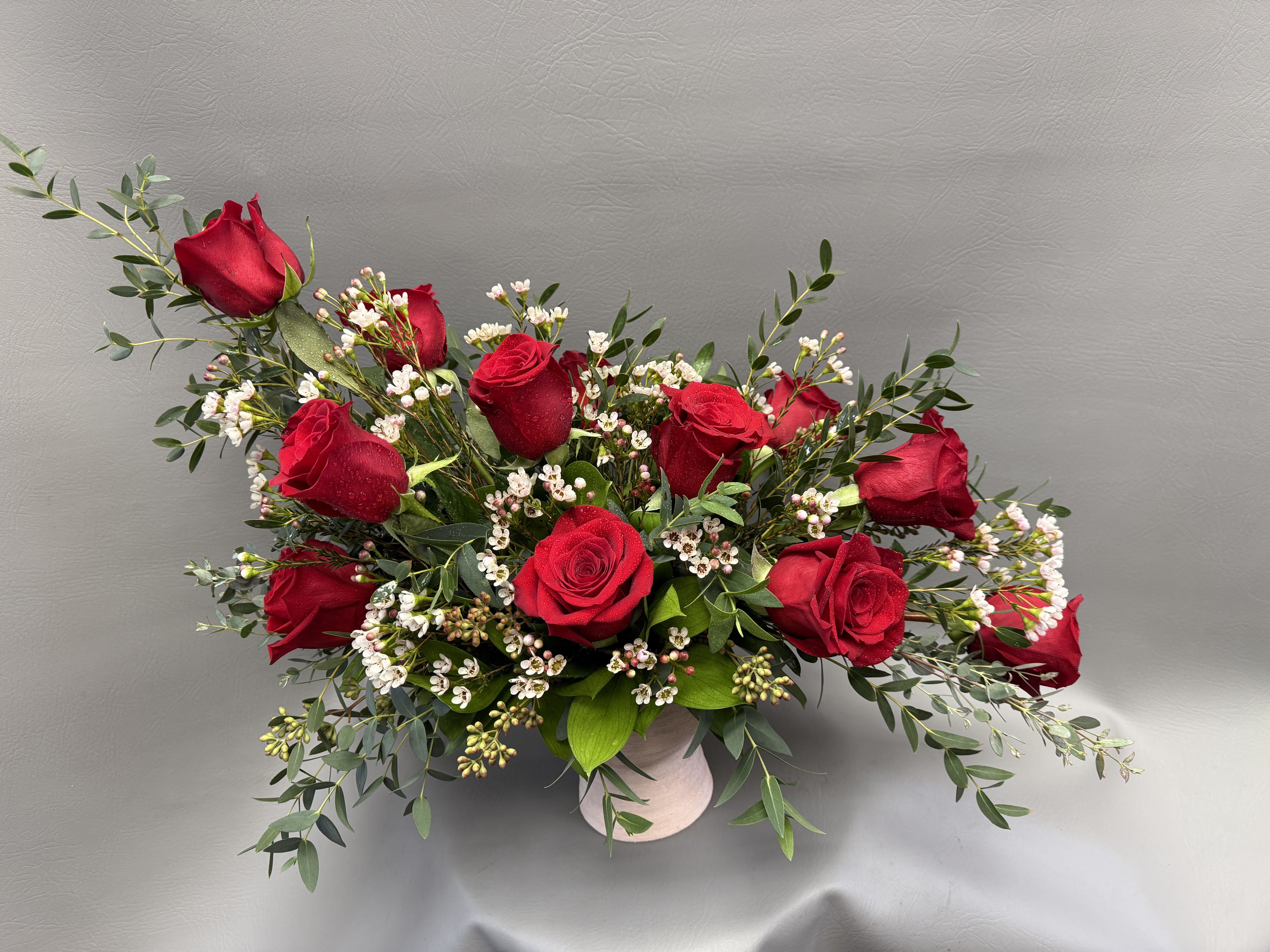 Red roses arranged in a low white vase with small white filler flowers