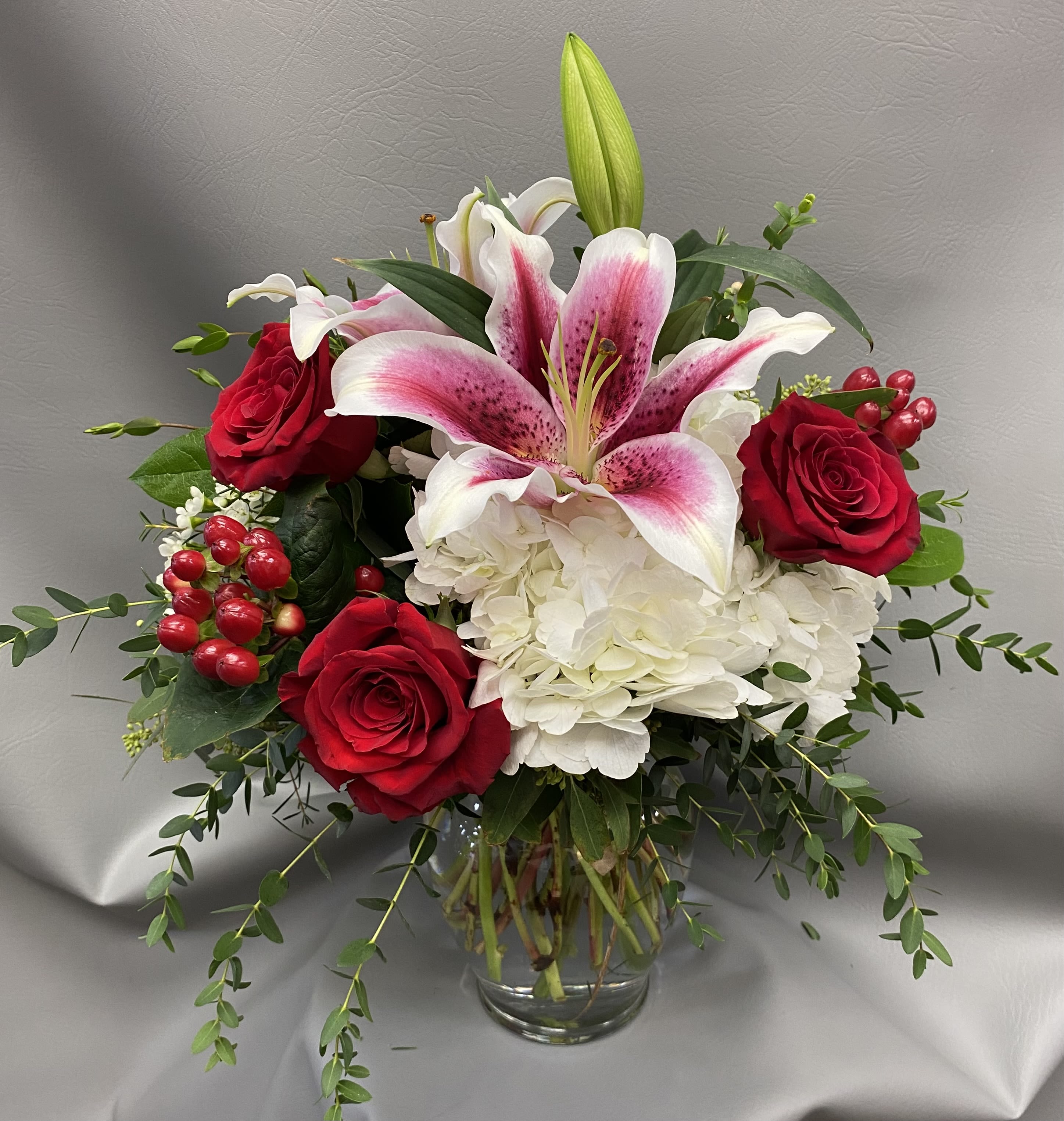 Red roses and white lilies in a glass vase with white hydrangea