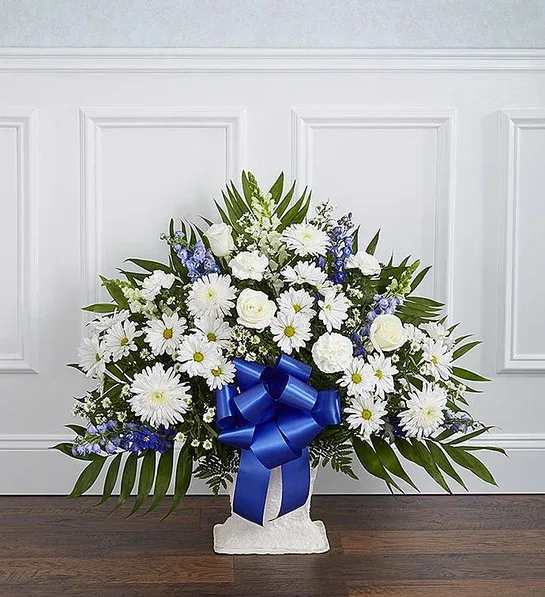 White and blue floral standing spray with a large ribbon on a pedestal.
