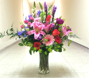 Tall mixed bouquet of pink lilies, roses, and purple flowers in a glass vase