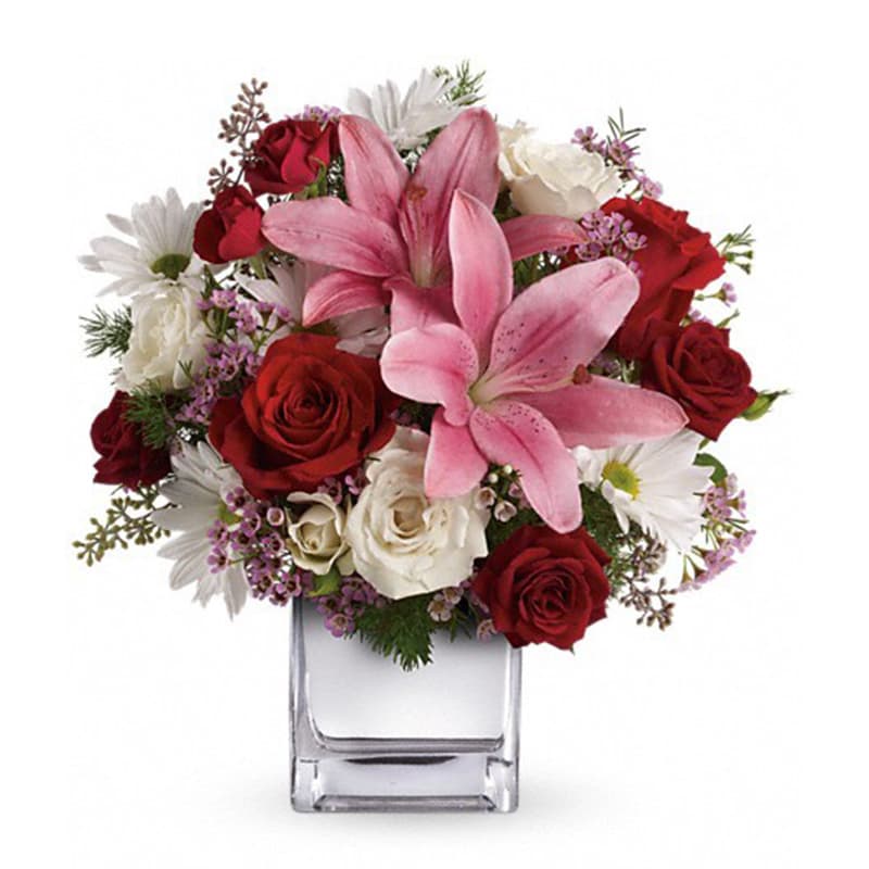 Bouquet of pink lilies, red and white roses, and white daisies in a clear glass vase