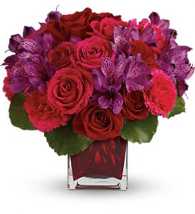 Red roses and purple flowers arranged in a clear square vase