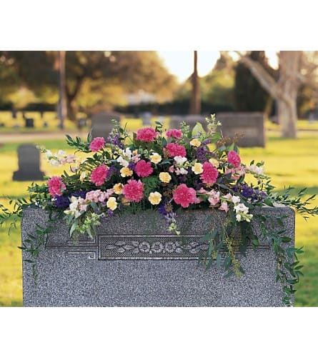 Cemetery saddle arrangement with pink, yellow, and white flowers on a gray headstone