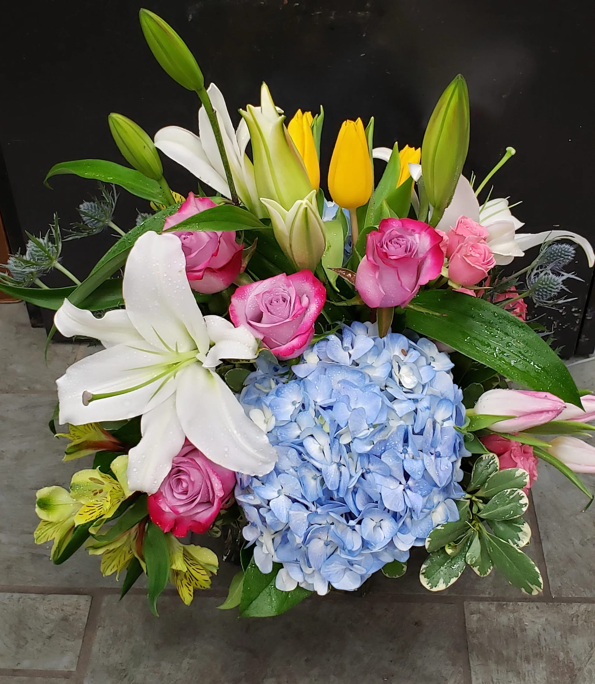 Bright mixed arrangement with pink roses, white lilies, yellow tulips, and blue hydrangea