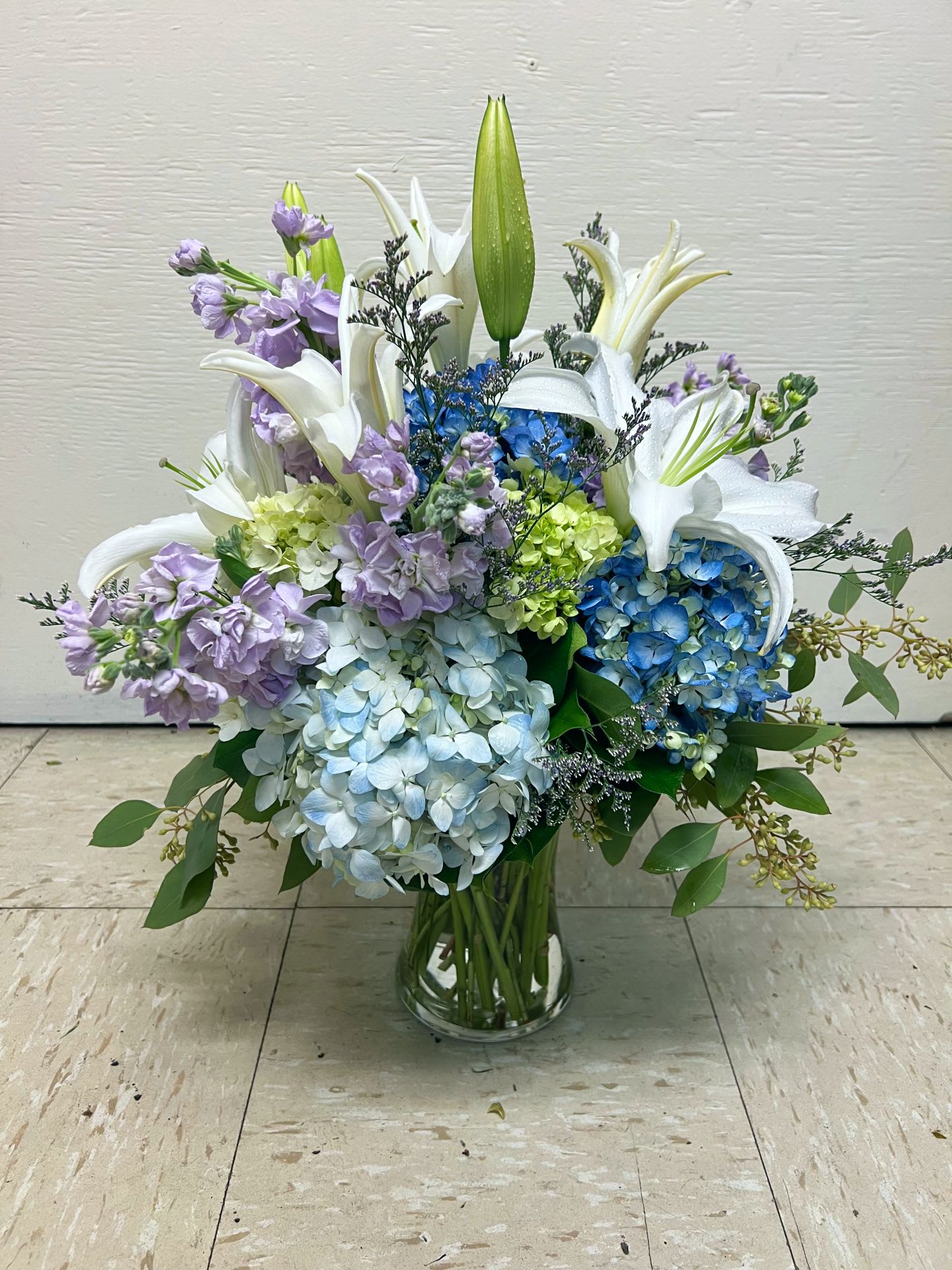 Blue and lavender hydrangea arrangement with white lilies in a glass vase