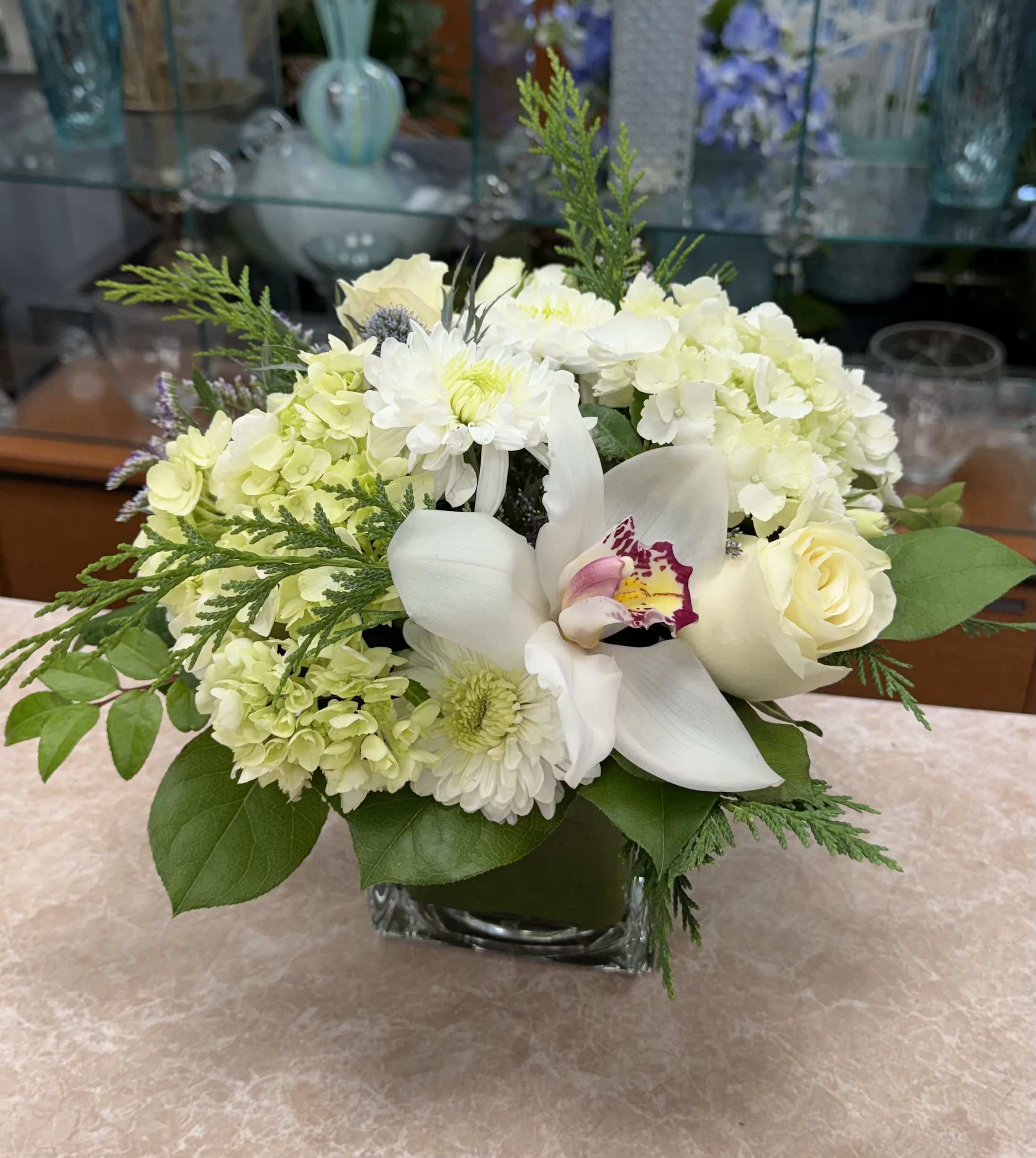 White and pale green floral arrangement in a square glass vase