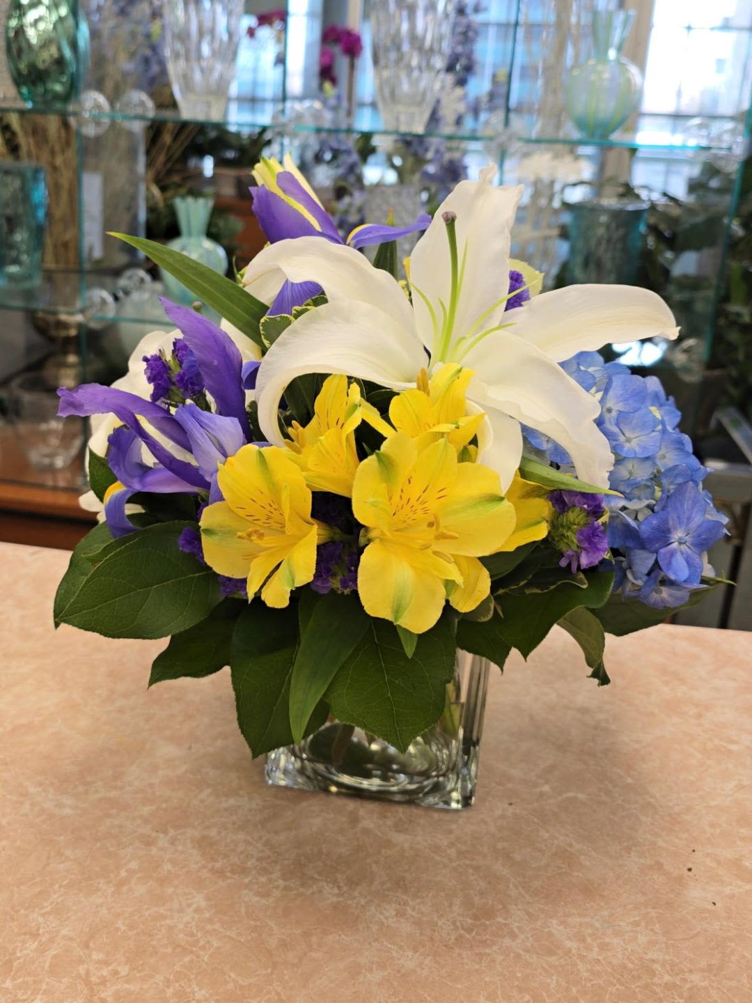 Mixed bouquet of white lilies, yellow alstroemeria, and purple iris in a glass vase