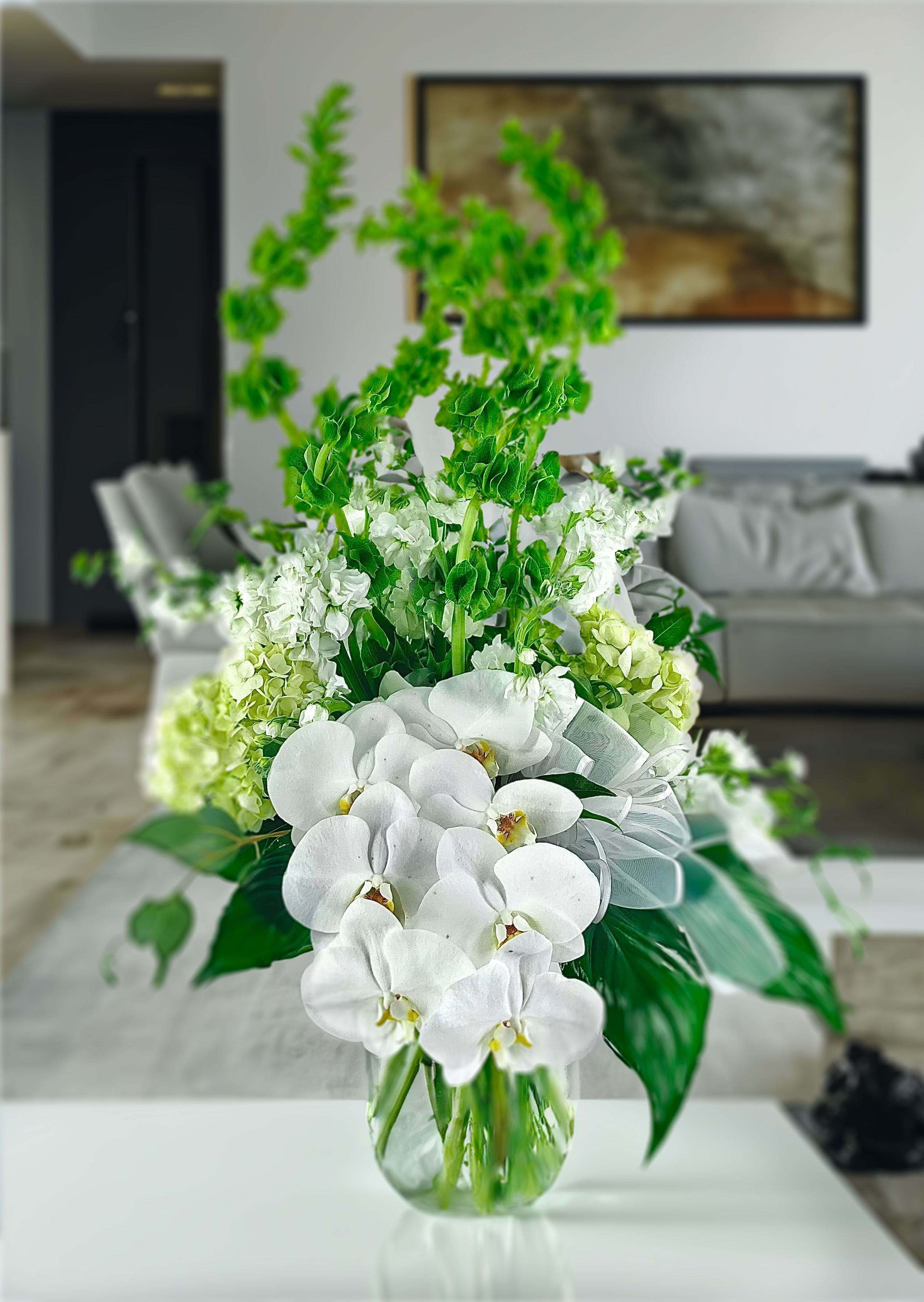 White orchids and green flowers in a clear glass vase