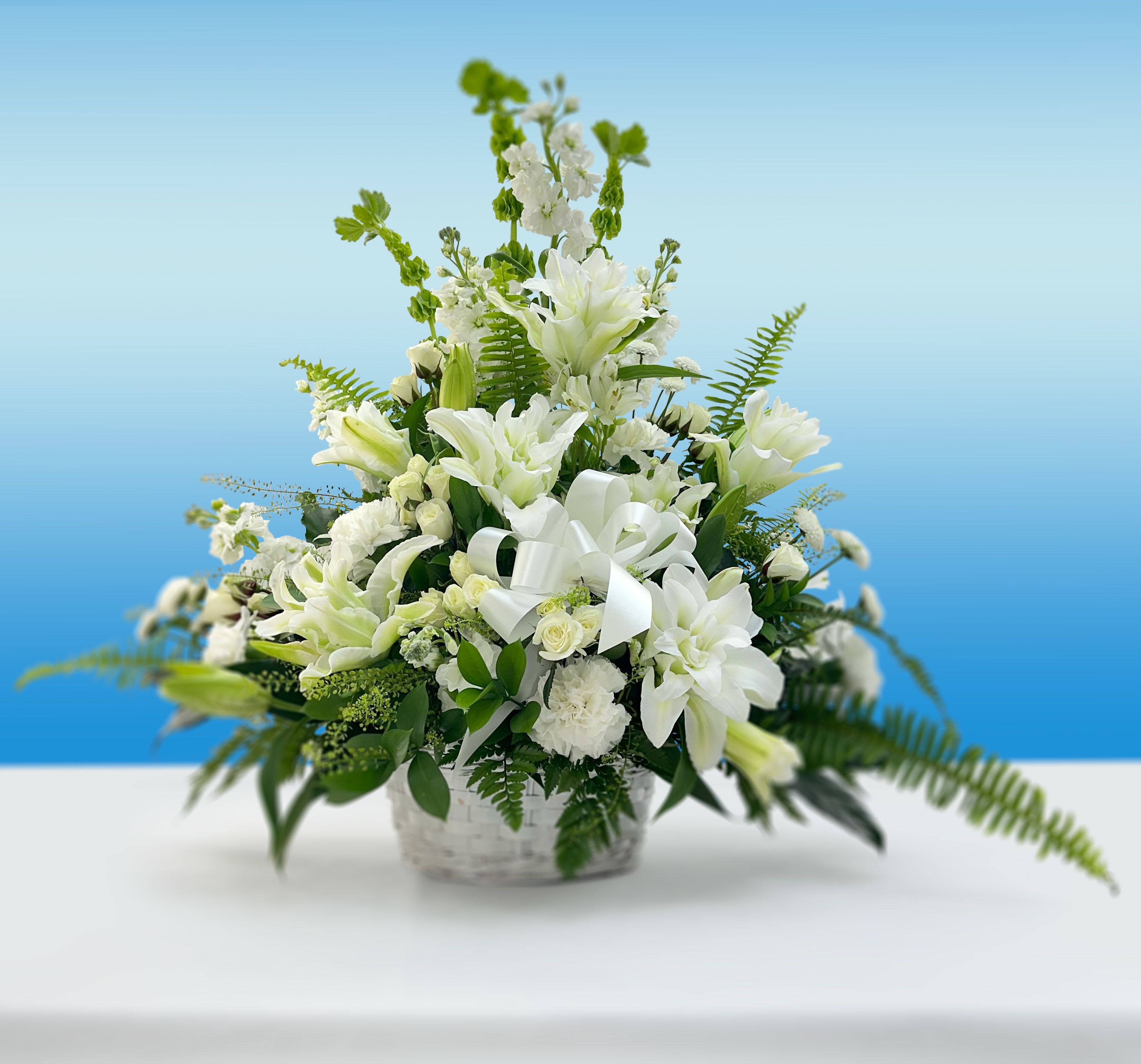 White lilies and roses arranged in a basket with a white ribbon