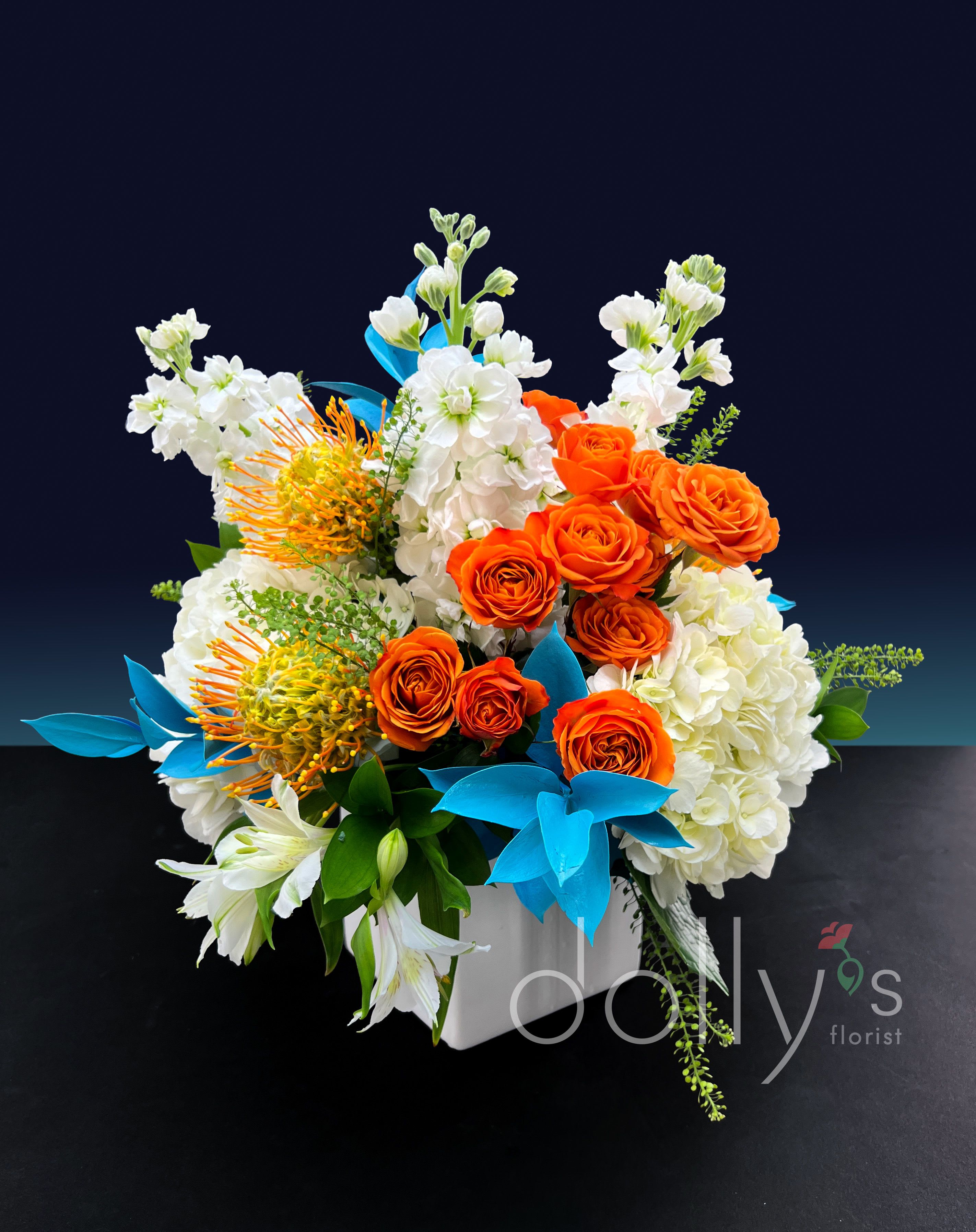 Orange roses and white flowers arranged in a white box with blue accents