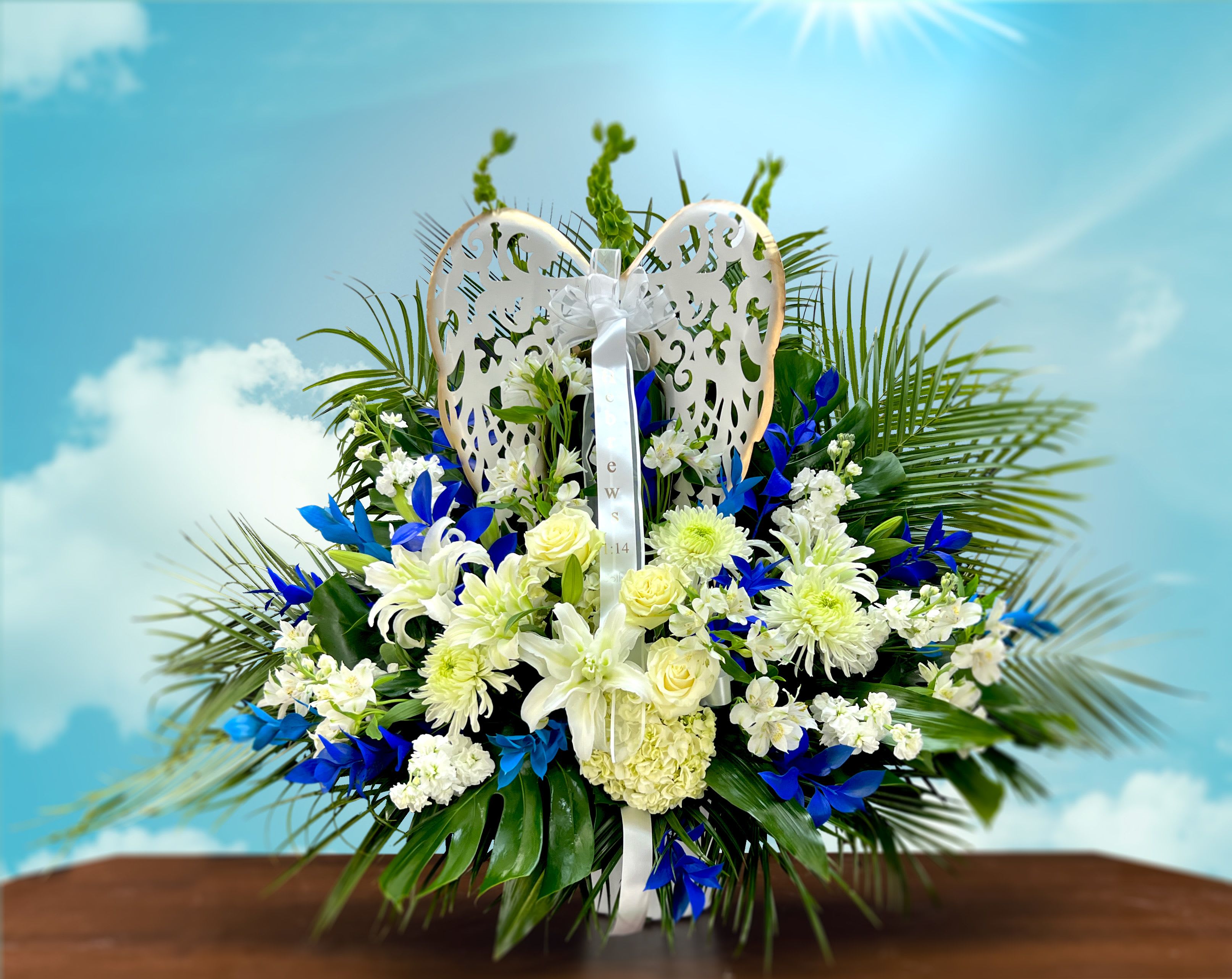 White and blue floral arrangement with a decorative angel wing topper