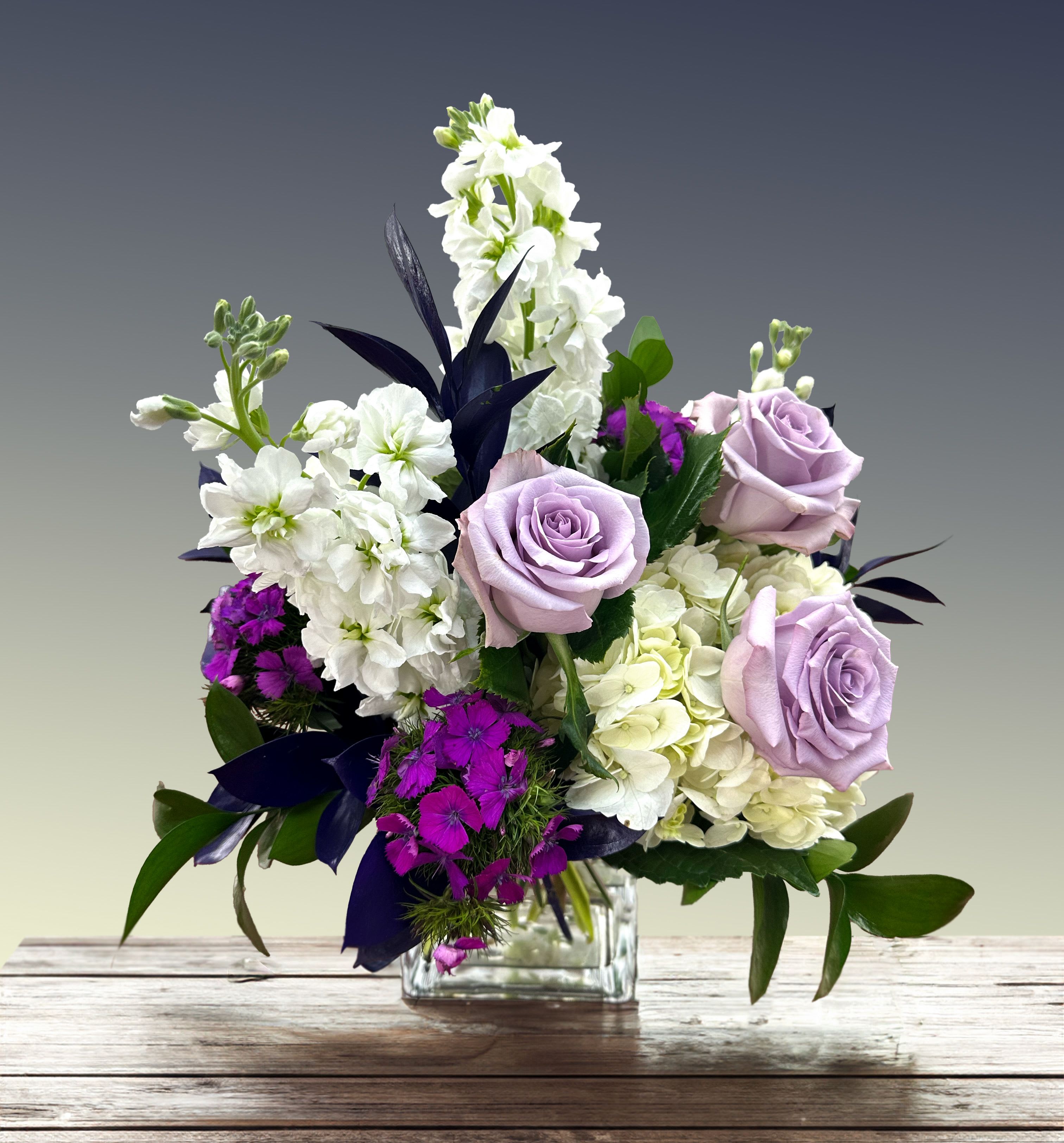 Lavender roses and white flowers in a clear glass vase