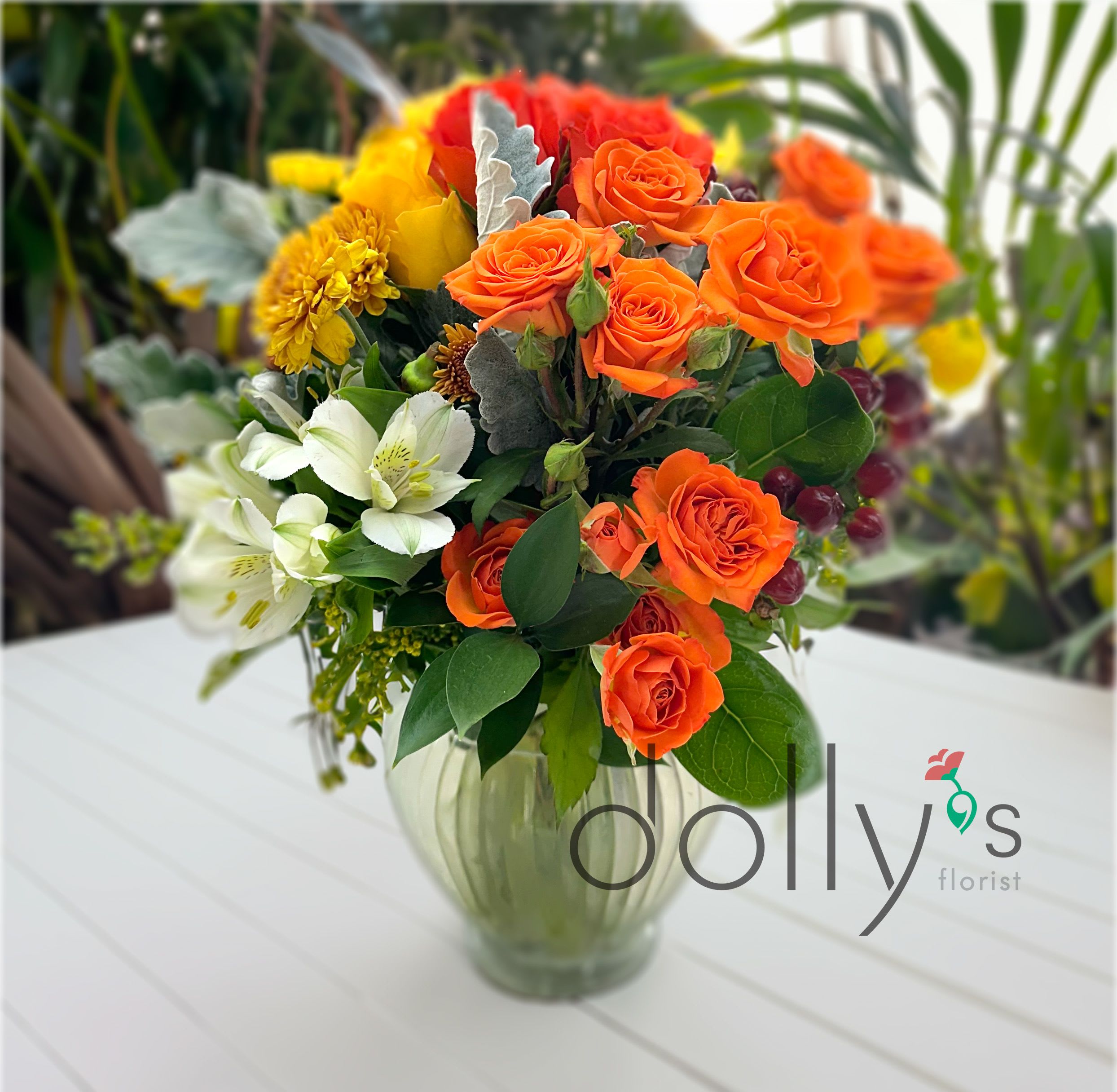 High-Key Hues - Vibrant clusters of orange roses take center stage in this mixed bouquet, balanced by sunny yellow chrysanthemums and crisp white alstroemeria-a high-energy flower arrangement perfect for a birthday, Mother's Day, Father's Day, or a thoughtful just‑because gift. The warm oranges and yellows feel joyful and celebratory while the white blooms add freshness and light, so the person you're gifting will feel genuinely noticed and cheered.  Arranged in a ribbed clear glass vase that showcases the stems and keeps the look classic and approachable, High-Key Hues combines roses, chrysanthemums, and alstroemeria for a textured, layered appearance. The compact design works well on a bedside table, desk, or dining table; colors read bright and welcoming in natural light and bring an autumnal glow when used for seasonal décor.  Send this as a congratulations bouquet, a get-well lift, or a simple thinking-of-you surprise-it's the kind of arrangement that feels both celebratory and sincere. Vase included; enjoy the lively mix of mixed color, orange, yellow, white, and red tones that make an immediate, uplifting impression.
