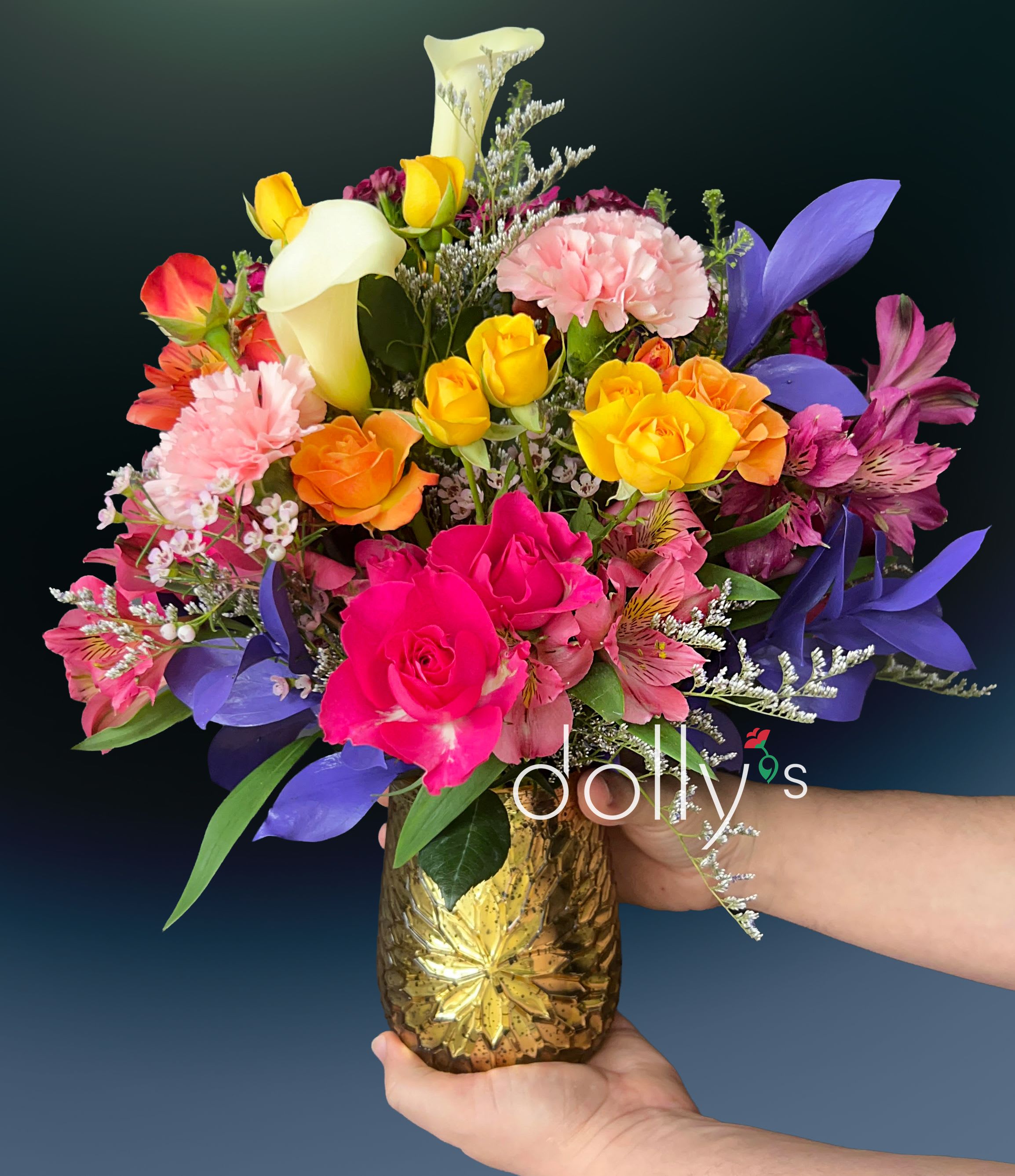 Cordially Invited - Vivid yellow calla lilies arch above a lush mix of roses and carnations in this colorful flower arrangement, a cheerful choice for a birthday bouquet, Mother's Day gift, or to say congratulations. The lively palette-hot pink and red roses, peach and orange roses, bright pink carnations, purple button chrysanthemums and deep purple irises-creates an energetic, celebratory impression that will make the person you're thinking of feel genuinely seen and celebrated.  Striped orange‑pink alstroemeria, delicate alstroemeria accents, spray roses, small filler blooms and berries add texture and movement throughout the design. The flowers are gathered in a warm gold finish with a starburst pattern that gives the arrangement contemporary sparkle and sturdy presence on a table or mantel. Sized to brighten any room, this arrangement is equally fitting for birthdays, anniversaries, get well wishes, thank yous, or "just because" moments-seasonally appropriate for Mother's Day, winter holidays, and autumn celebrations while remaining perfect year‑round.
