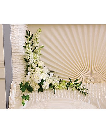 White floral arrangement on a draped casket with a fan backdrop