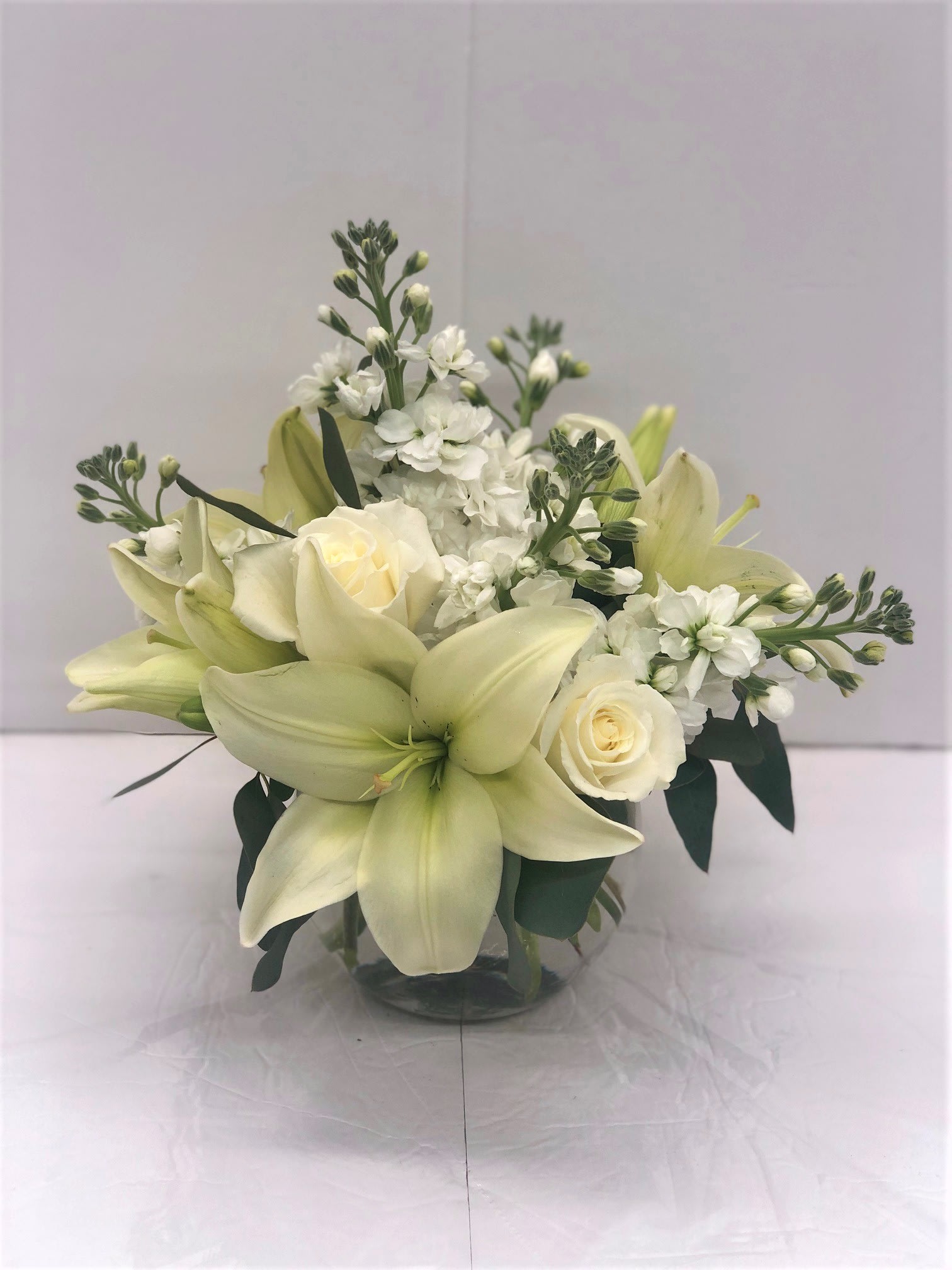 White lilies and roses arranged in a clear glass vase