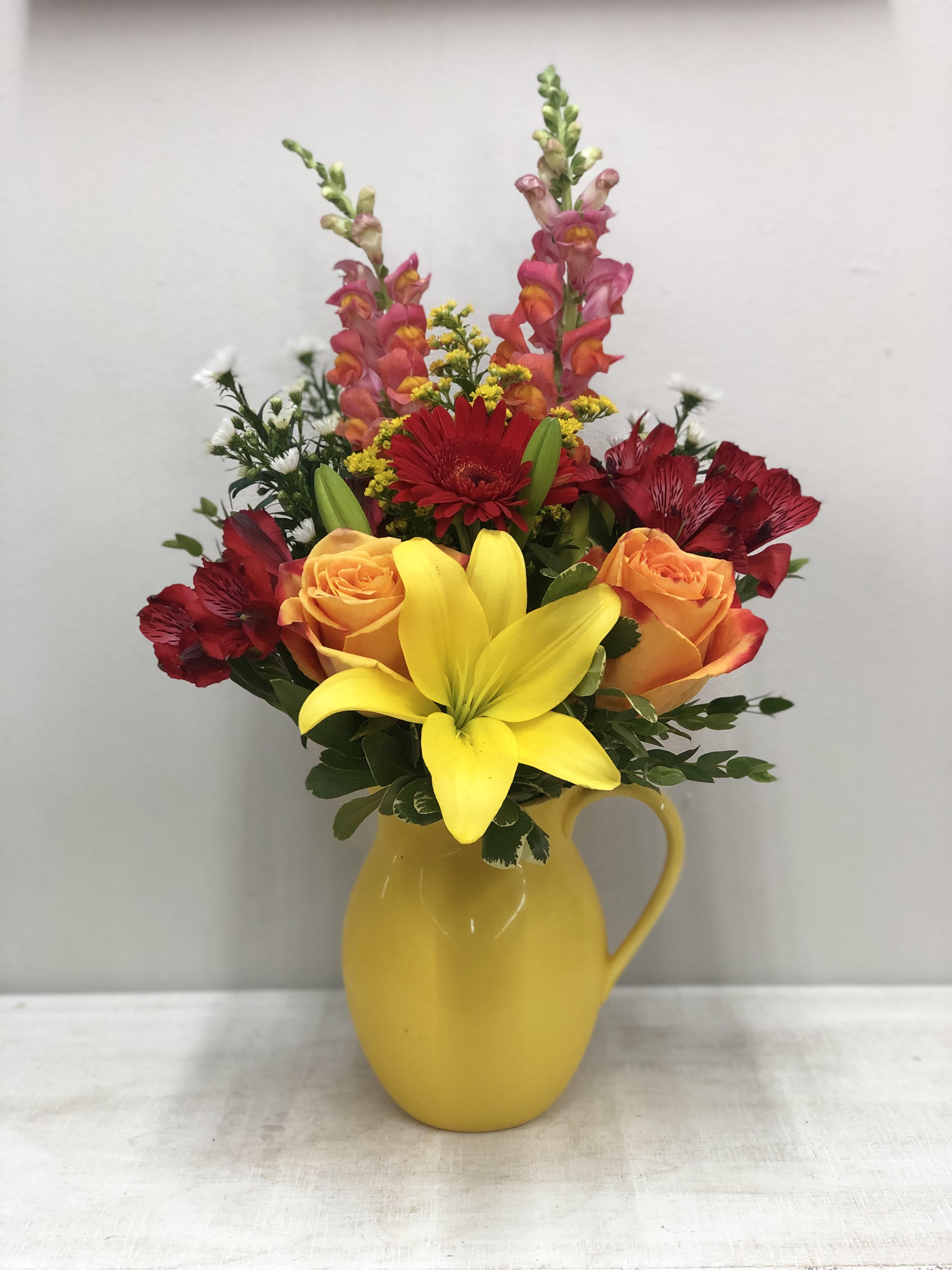 Colorful bouquet in a yellow pitcher vase with roses, lilies, and snapdragons