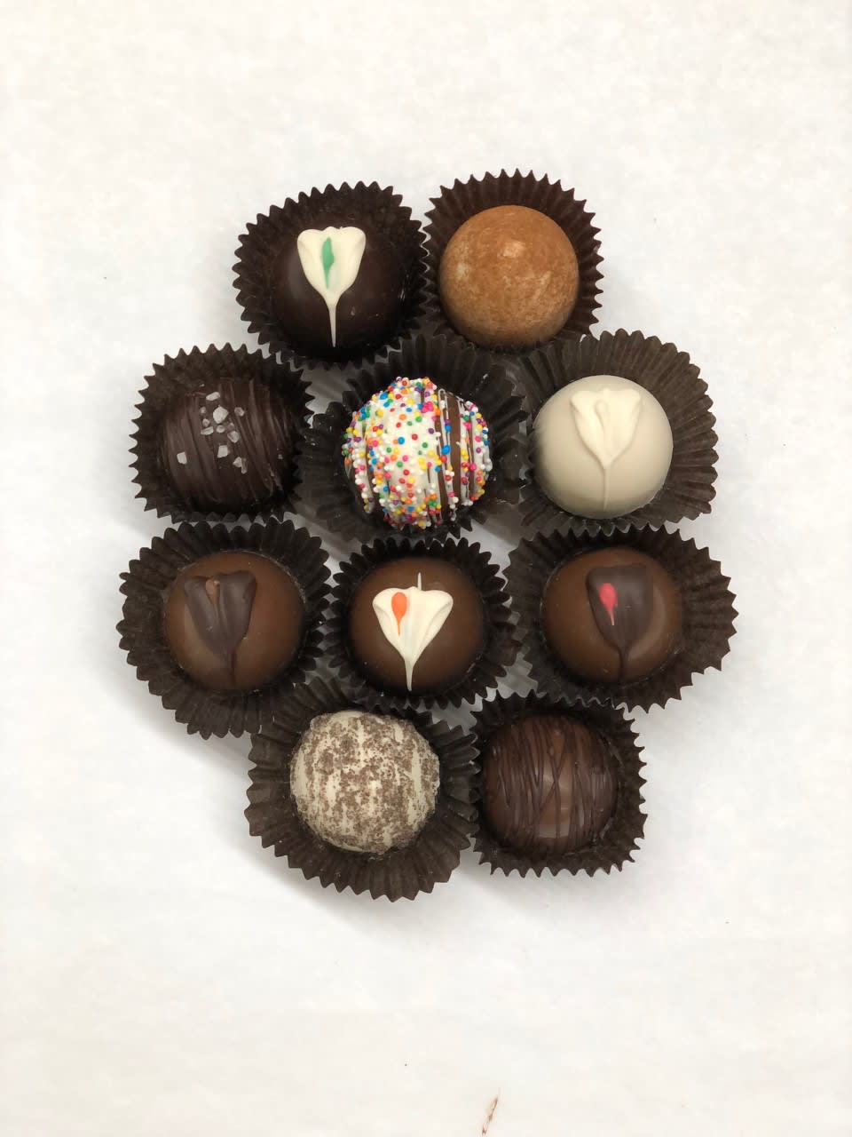 Assorted chocolate truffles with varied toppings arranged in a circle on a white background