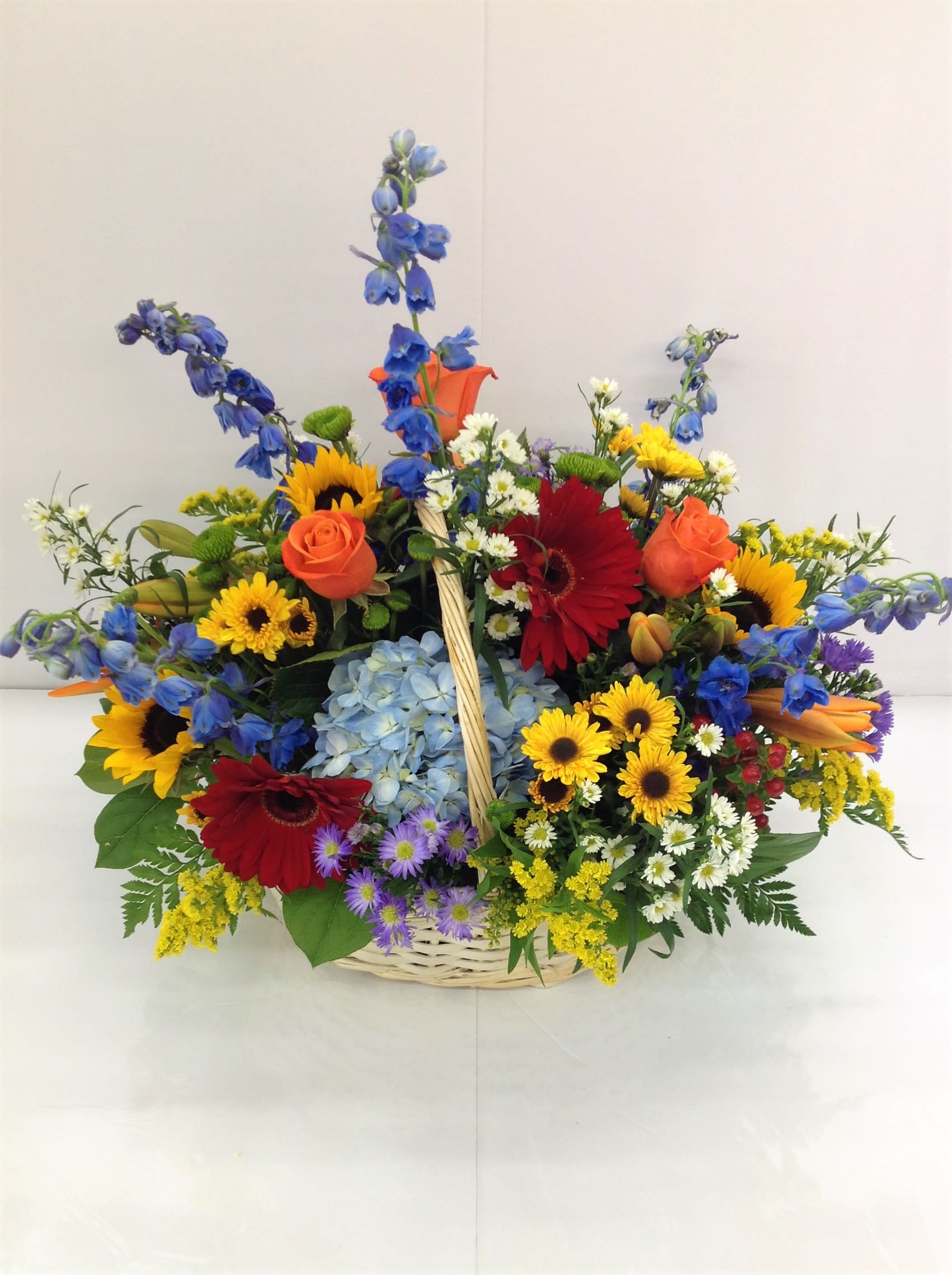 Colorful mixed flower basket with roses, gerberas, sunflowers, and blue delphinium