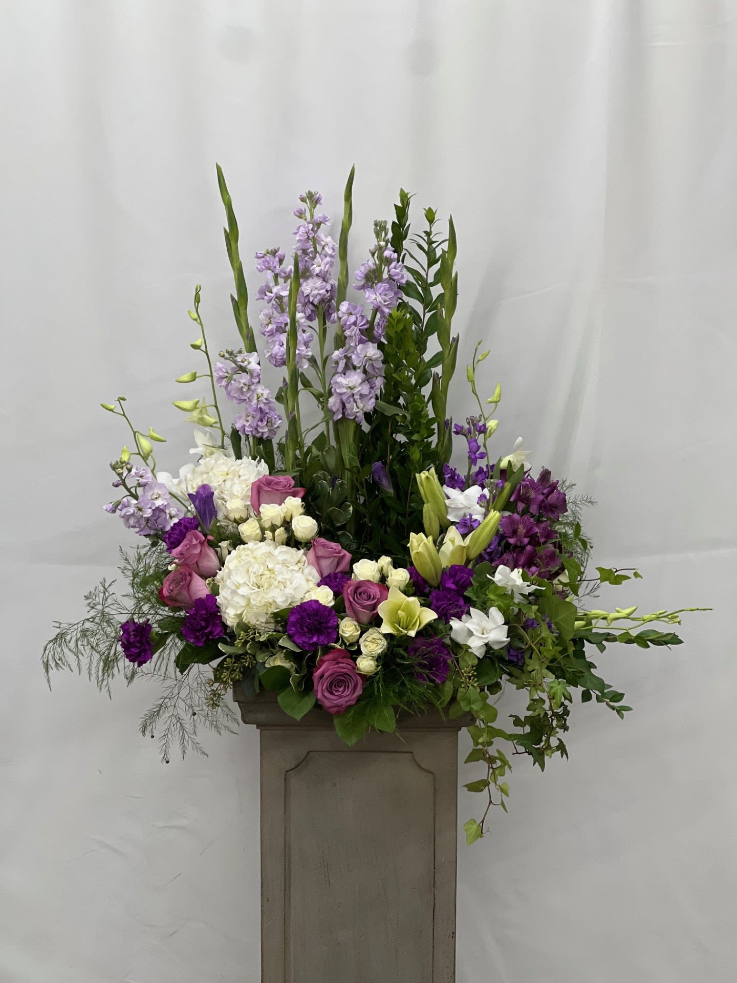Tall floral arrangement with purple, white, and pink blooms in a pedestal container