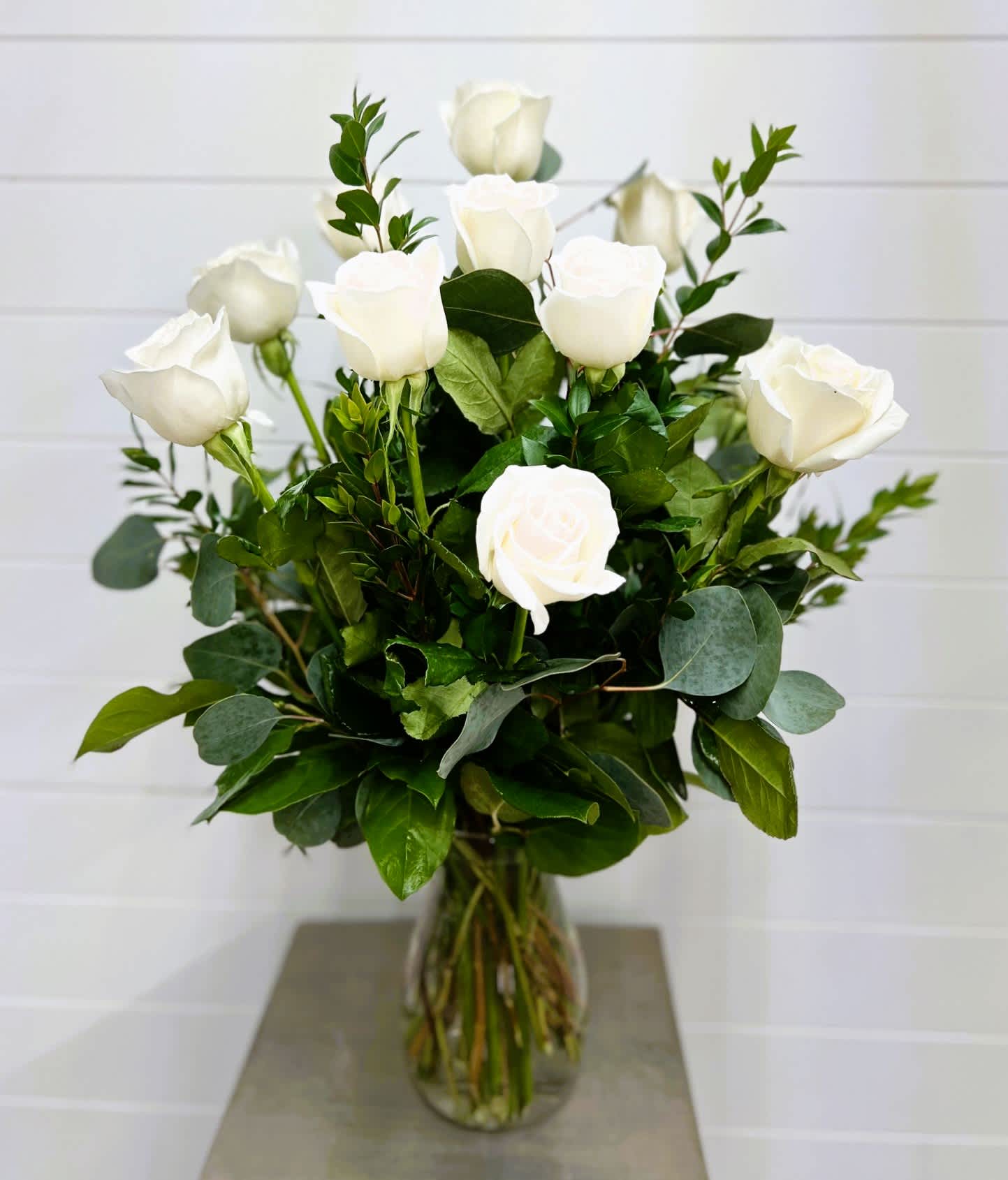White roses arranged in a clear glass vase with mixed greenery