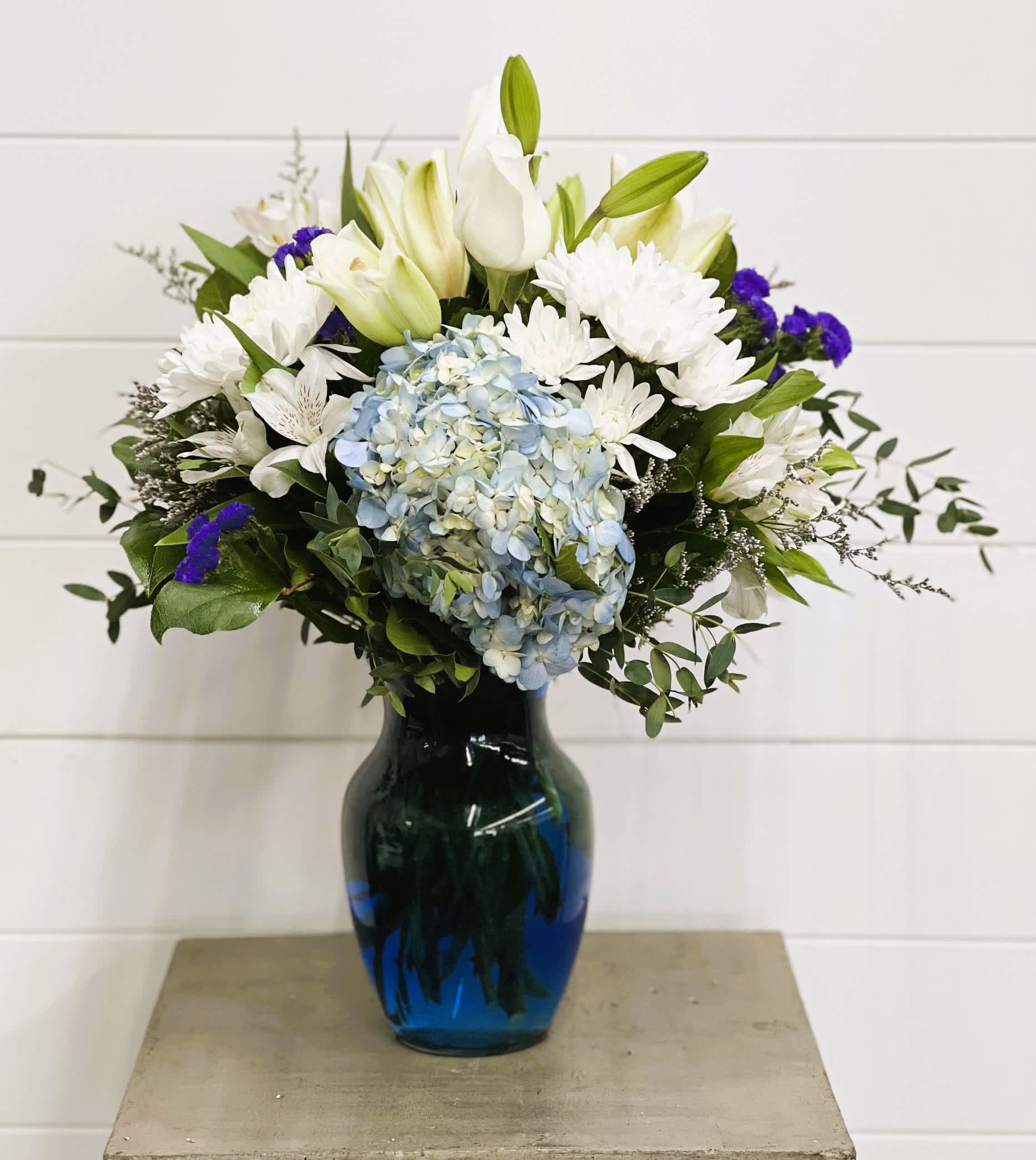 White lilies and daisies with blue hydrangea in a blue vase