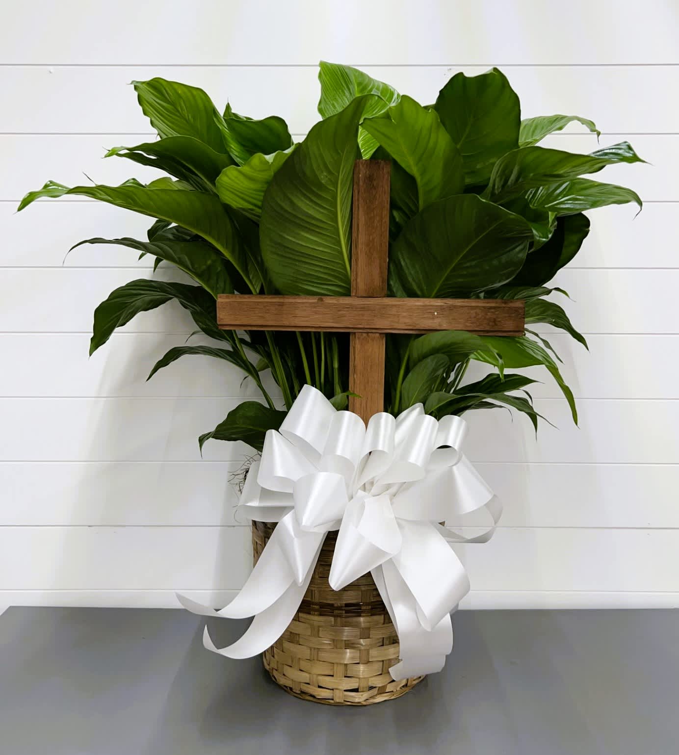 Potted green plant with a wooden cross and white ribbon in a woven basket