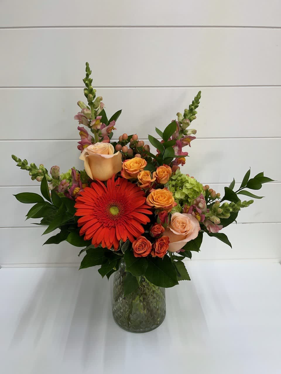 Mixed bouquet with orange gerbera daisies and peach roses in a glass vase