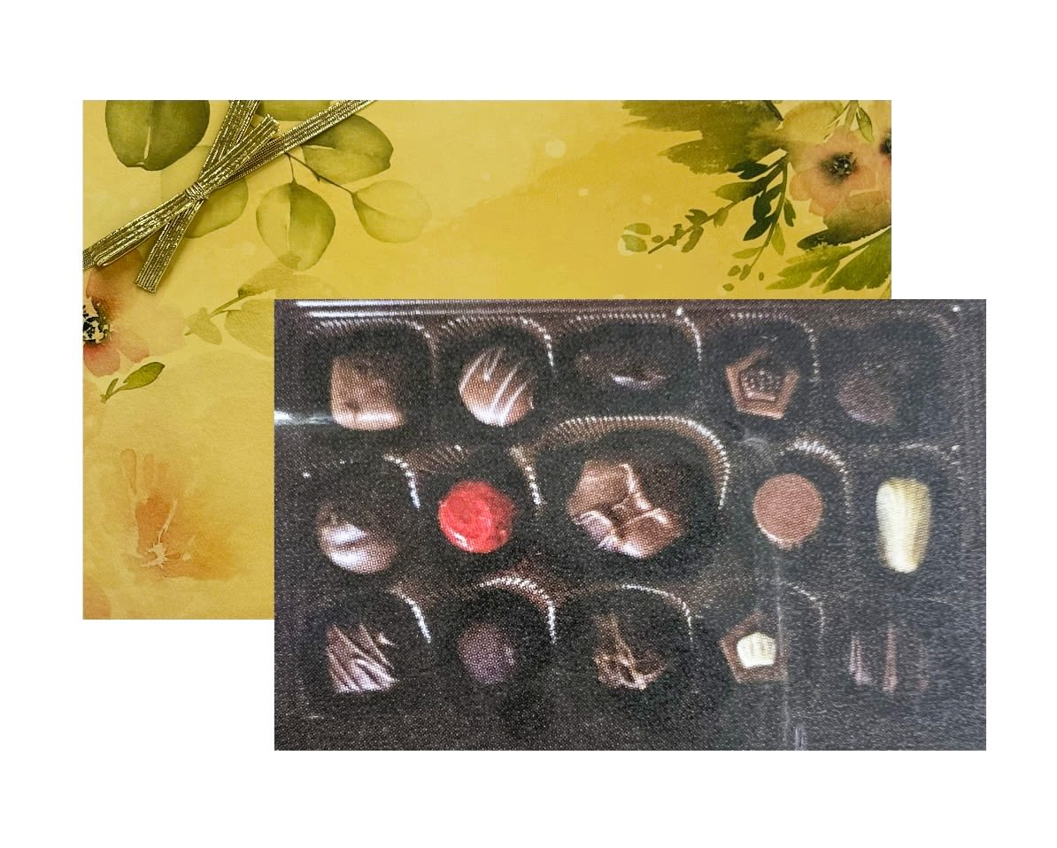 Rectangular gift box of assorted chocolates with a yellow floral lid and gold ribbon.