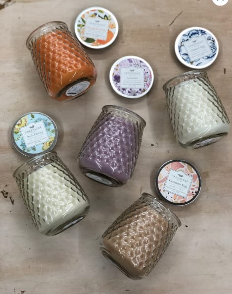 Assorted colored jar candles with patterned lids arranged on a light wood surface
