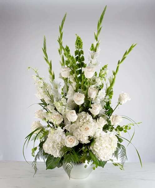 Sweet Comfort - An all white tribute, this funeral basket is pure and tranquil. Featuring a variety of white flowers and greenery, this design reaches for the sky and evokes a feeling of peace upward and outward. 