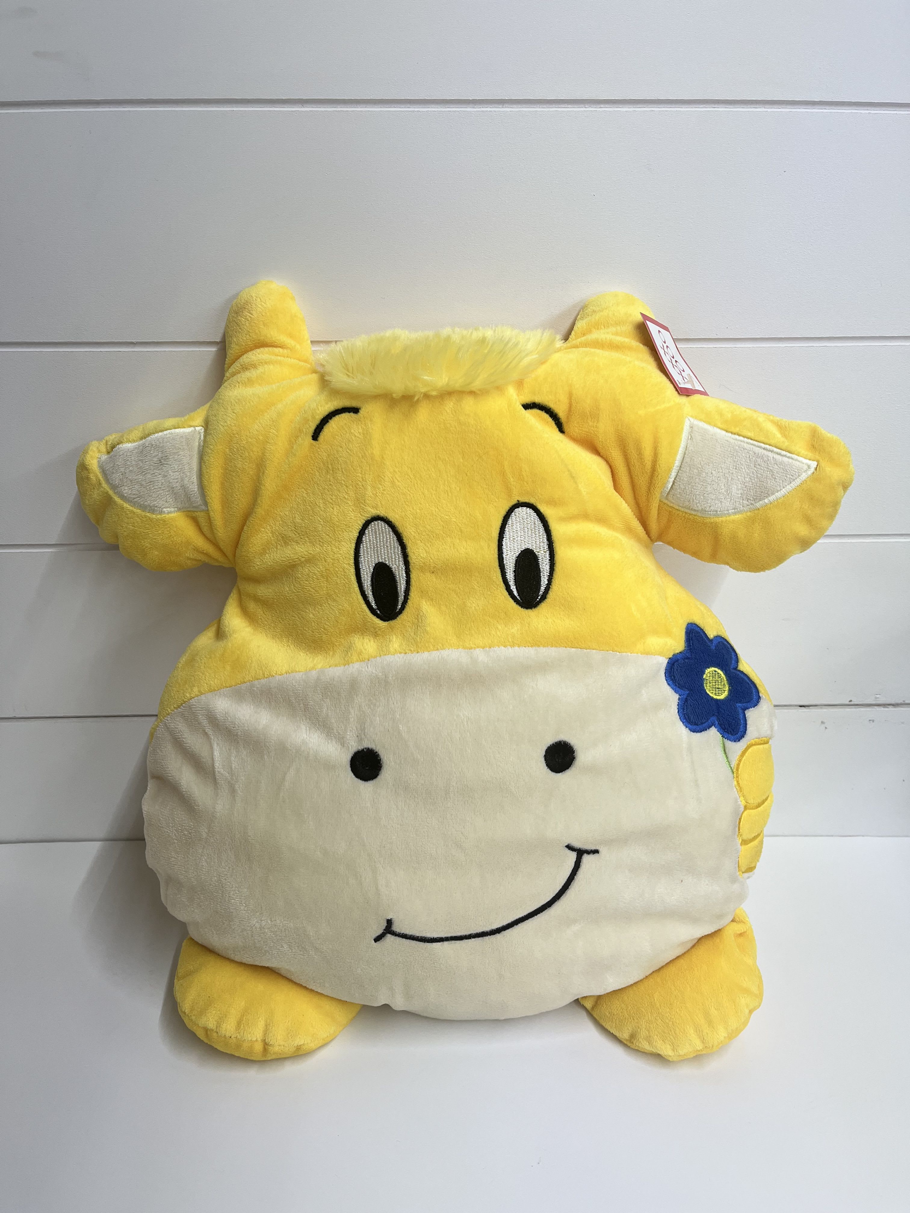 Yellow plush cow pillow with a smiling face and blue flower detail