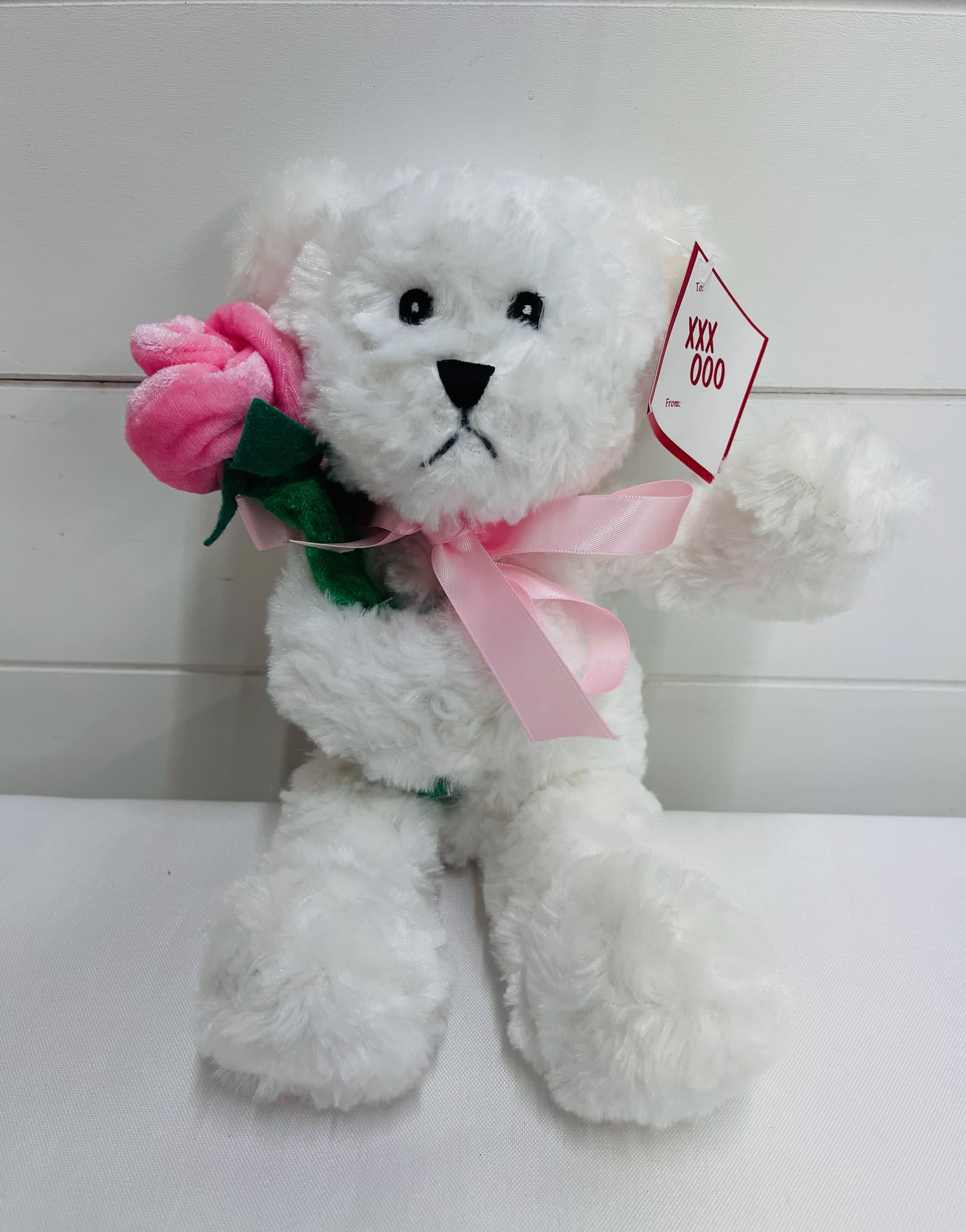 White plush teddy bear holding a pink fabric rose with a pink ribbon and gift tag