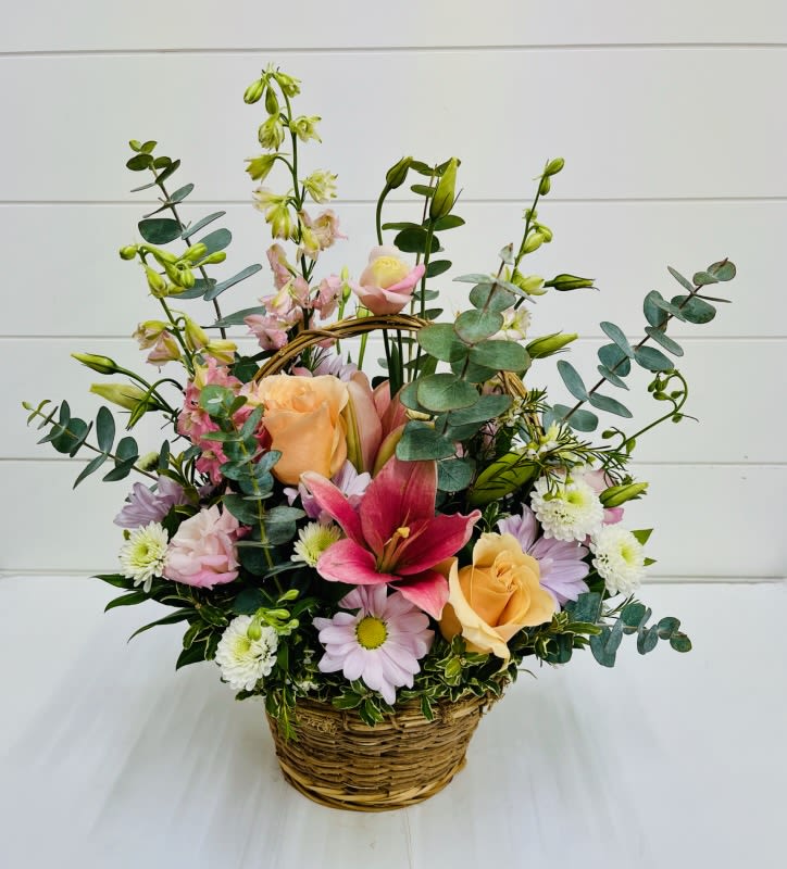 Pastel Garden  - Soft, romantic, and full of spring charm, our Pastel Garden Basket is a beautifully arranged collection of delicate seasonal blooms. Designed in a classic basket, this arrangement features soothing lavender daisies, elegant pink lilies, and soft peach roses, complemented by airy pink delphinium and graceful lisianthus. White cushion poms add texture and fullness, while eucalyptus brings a fresh, natural finish with its signature silvery greenery.  With its dreamy pastel palette and garden-inspired feel, Pastel Garden Basket is perfect for Easter celebrations, spring gifting, or simply brightening someone’s day.  We proudly offer local flower delivery to Smyrna, Marietta, Mableton, Austell, and Atlanta. Same-day delivery may be available depending on order time and product availability.  Substitution Policy: Due to seasonal and market availability, substitutions may be necessary. Any substitutions will be made with equal or greater value while maintaining the overall style, color palette, and design of the arrangement.