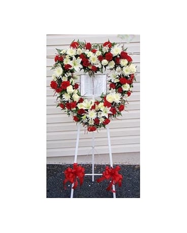 Heart-shaped red and white floral wreath on a stand with red bows