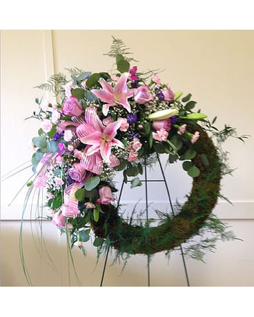 Pink lilies and roses arranged in a circular wreath on a stand