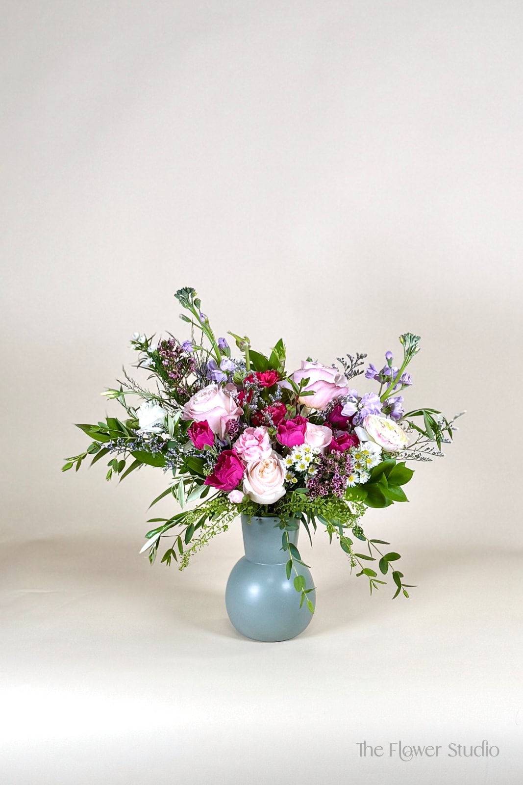 Pink and lavender roses, carnations, and daisies arranged in a matte blue vase.