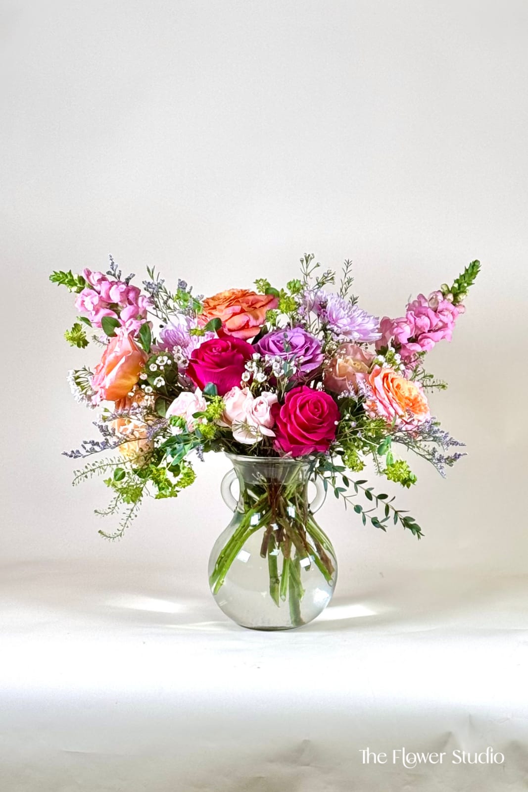 Mixed pink, purple, and orange flowers in a clear glass vase