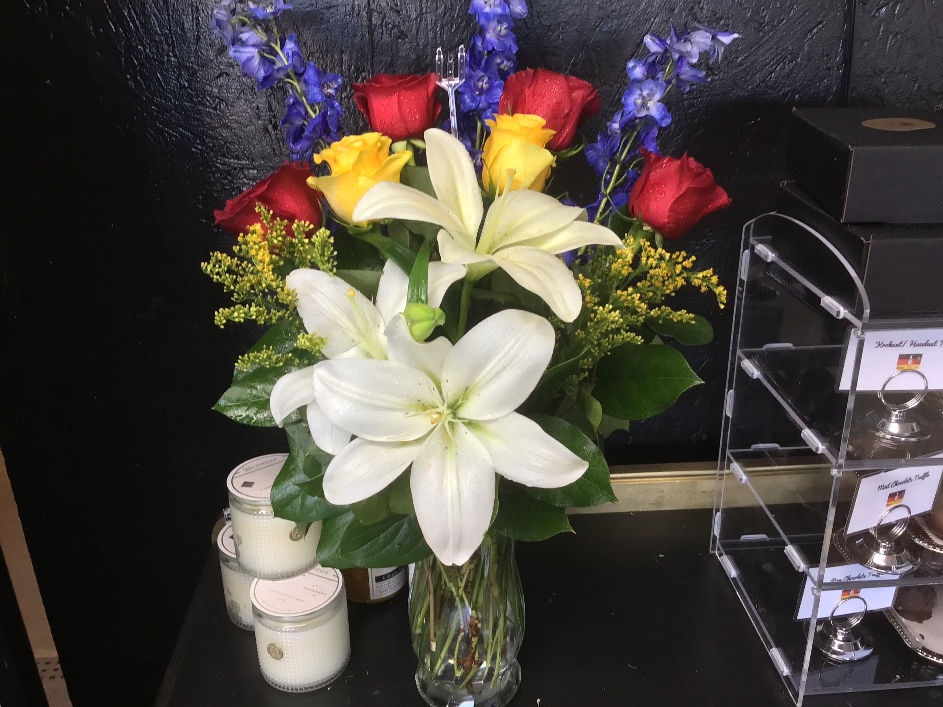 Bouquet of white lilies, red and yellow roses, and blue flowers in a glass vase