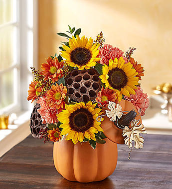 Pumpkin n’ Posies - One-sided arrangement with sunflowers; orange carnations ; daisy poms; accented with red painted solidago, myrtle, variegated pittosporum and dried lotus pods