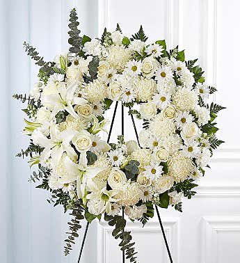 White funeral wreath on a black easel with lilies and roses